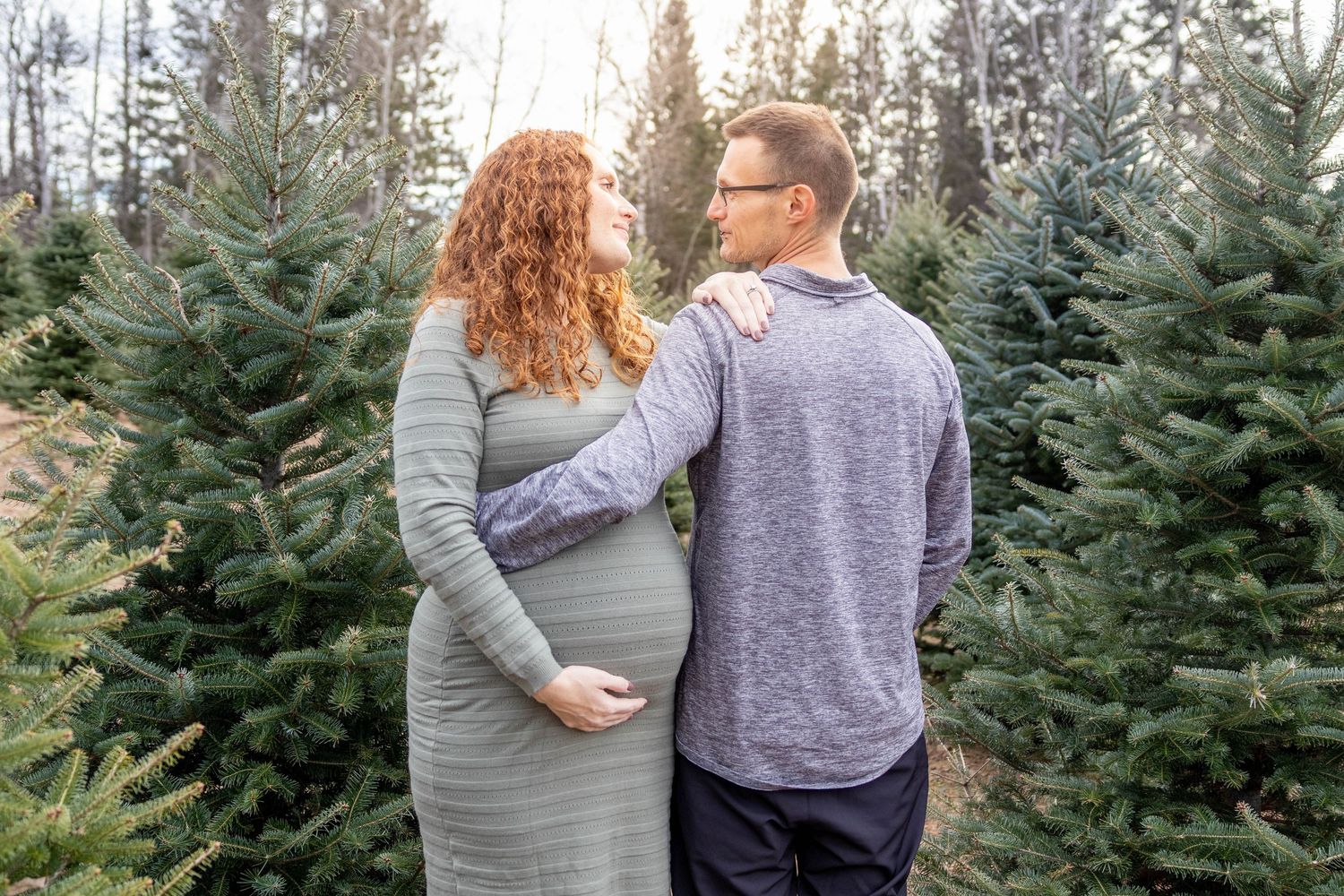 A couple browses evergreen trees at a Christmas tree farm on a winter afternoon.