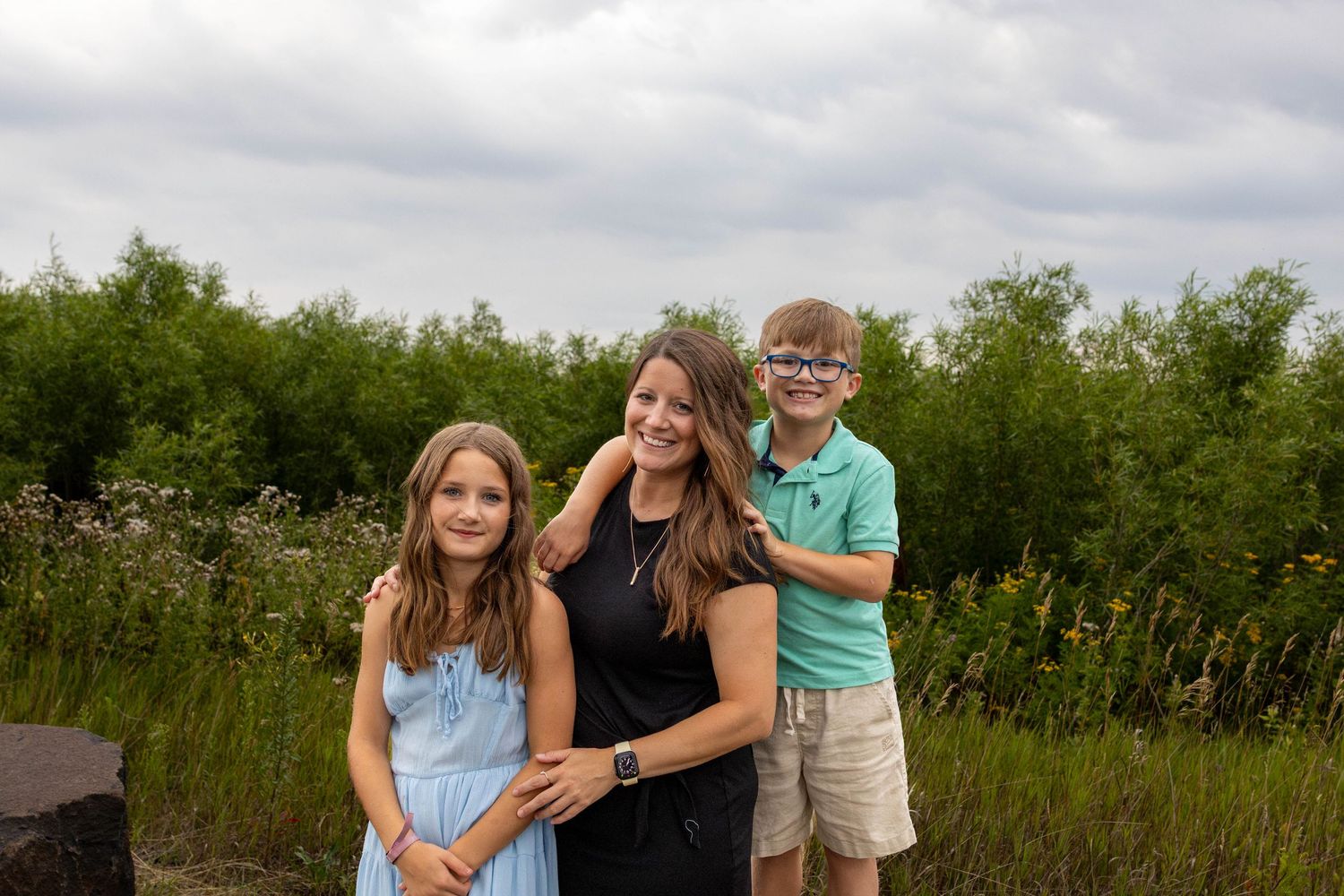 Candid outdoor family portrait shows joyful interaction in a natural meadow setting with green vegetation.