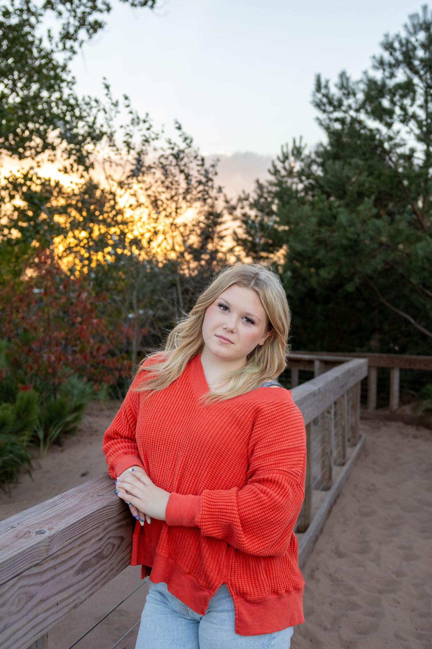 Outdoor portrait series at sunset showing someone in a bright coral sweater and jeans posing against wooden railings.