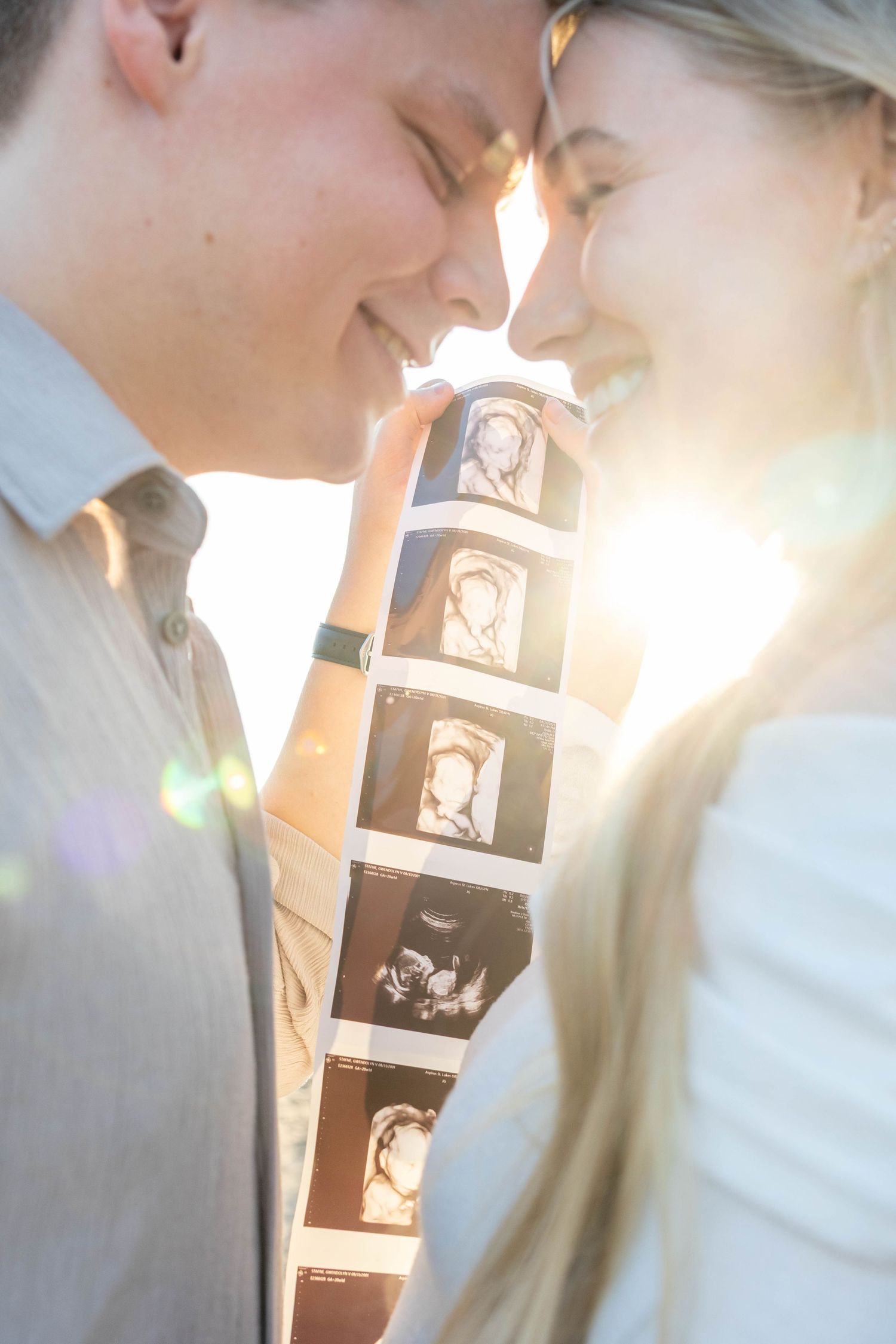 A romantic couple shares a tender kiss in soft sunlit lighting with a decorative wall panel in the background.
