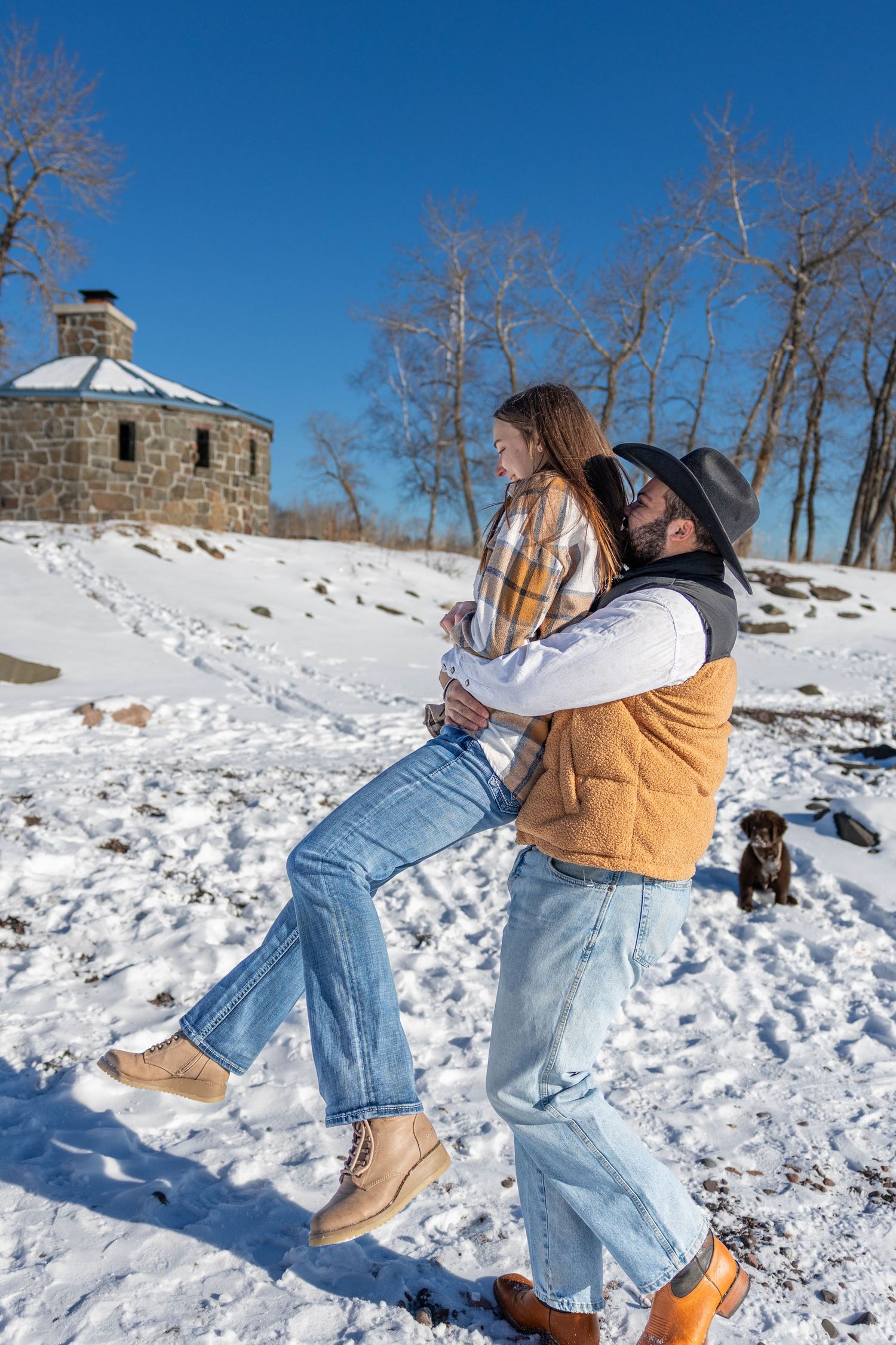 Couple dancing and twirling in the snow with a bright blue winter sky backdrop.