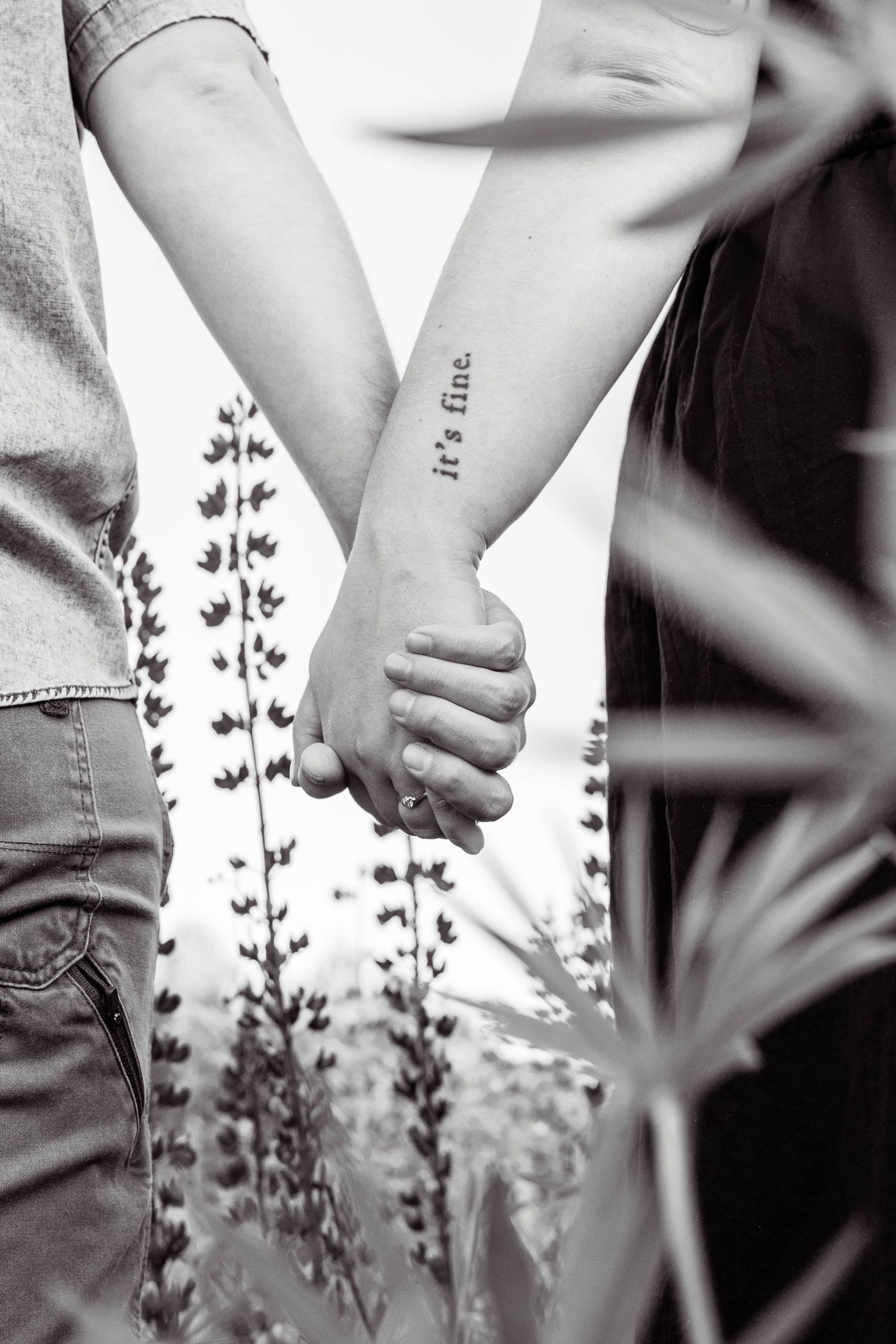 Black and white artistic photograph showing hands holding flowers against a soft background of lupine plants in bloom.