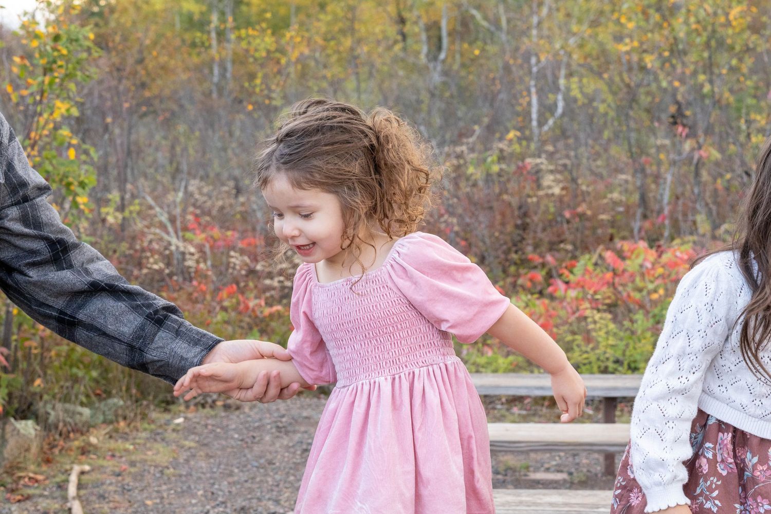 Children in pink dresses play and twirl together in an outdoor autumn setting with golden sunlight.