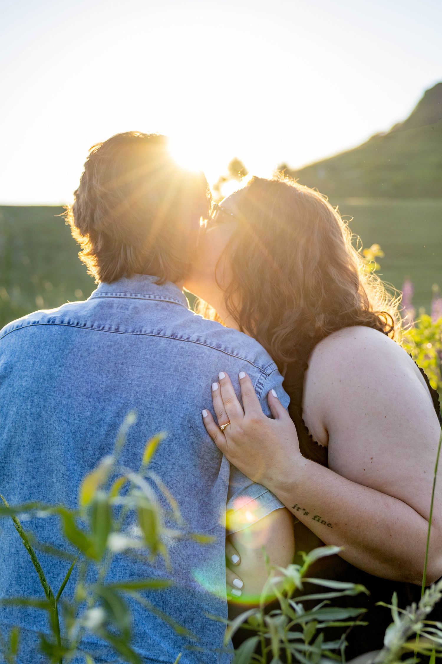 A couple shares an intimate moment at sunset with sunlight creating a golden backlit glow through their hair.