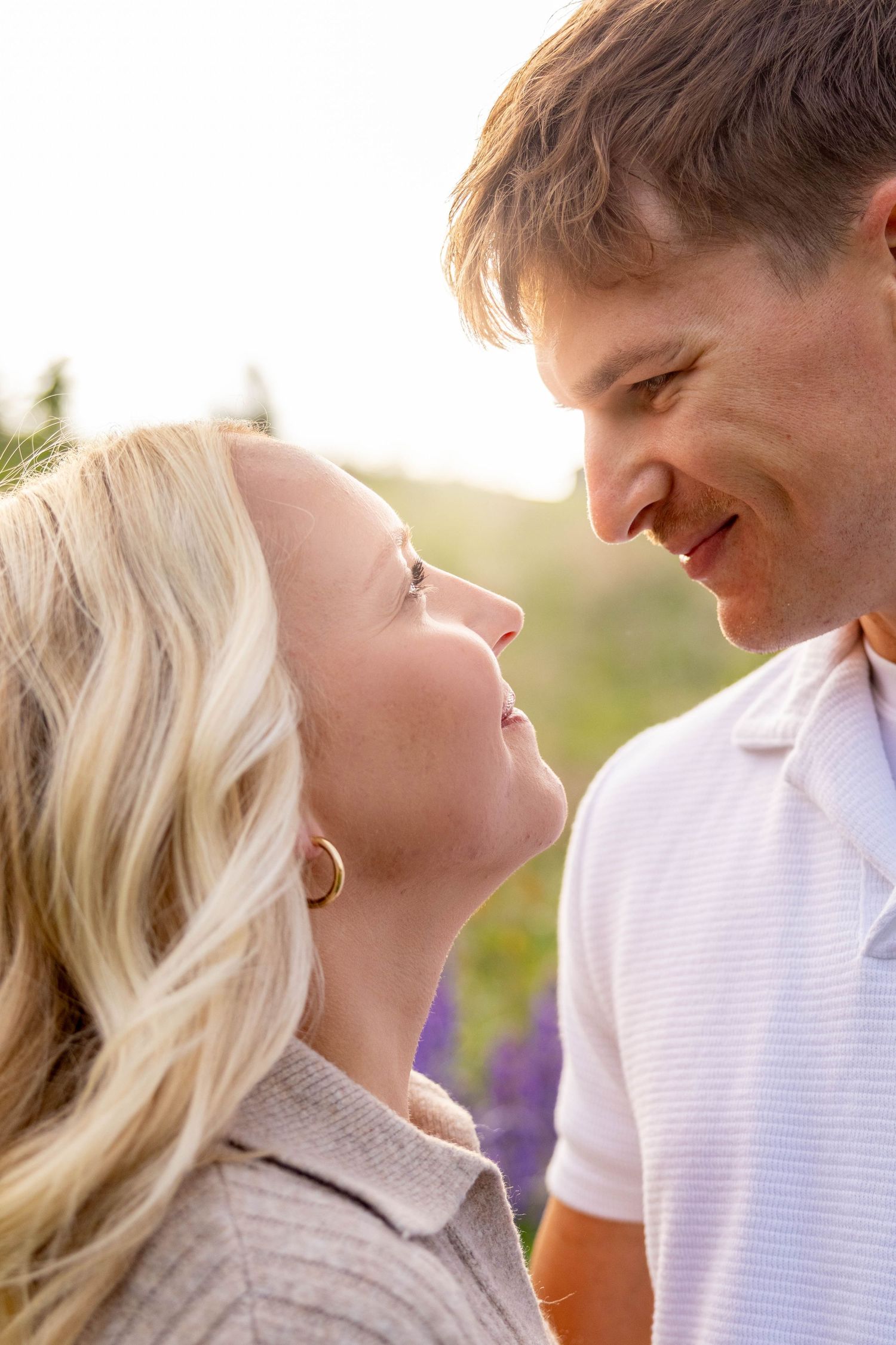 A couple shares an intimate moment together in a sunlit field with purple wildflowers.