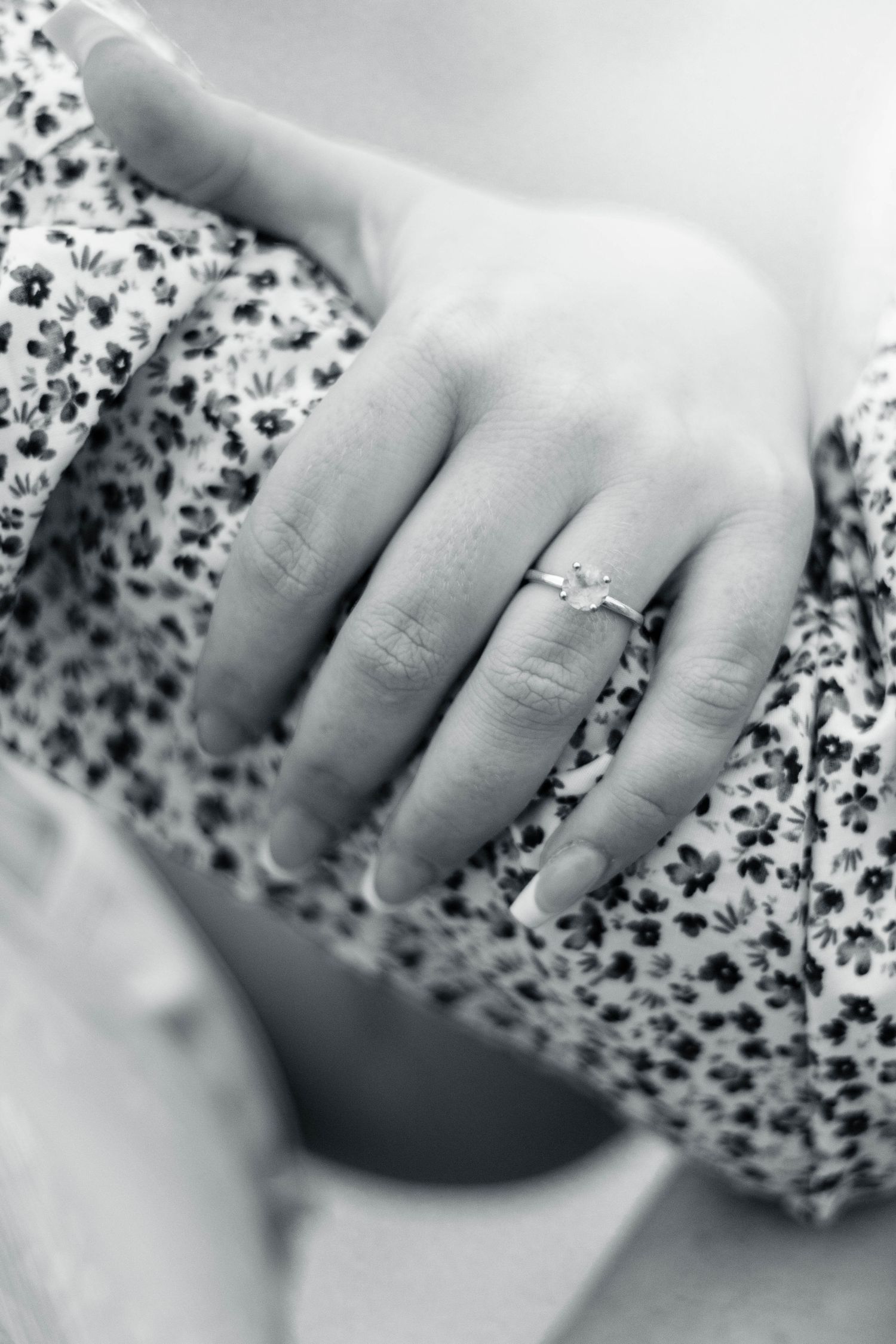 Close-up black and white image of fingers resting on a floral patterned fabric or surface.