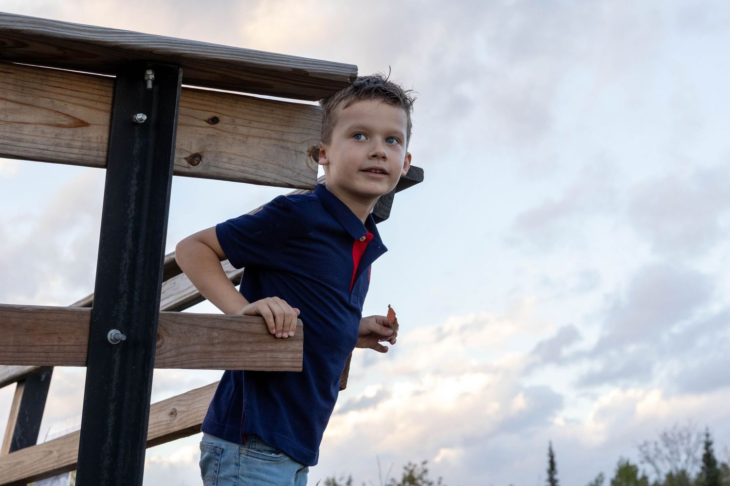 A wooden structure against a cloudy sky with people climbing and playing.