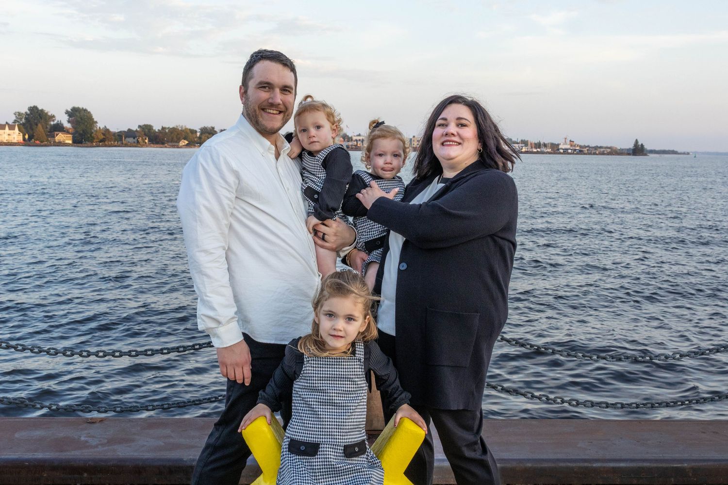 A family enjoys a scenic waterfront view from a dock during sunset.