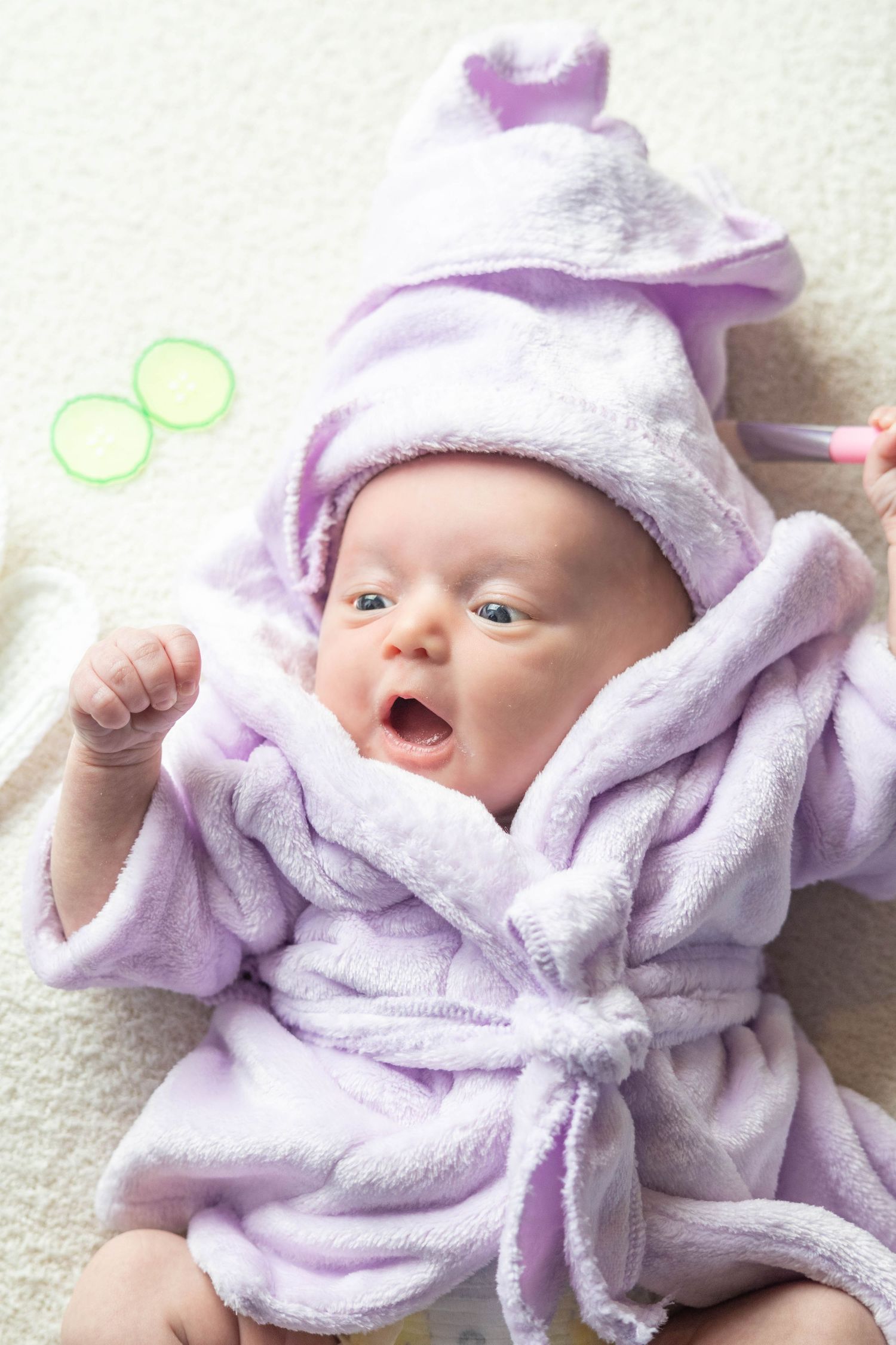 Happy baby in purple bathrobe lying on white background.