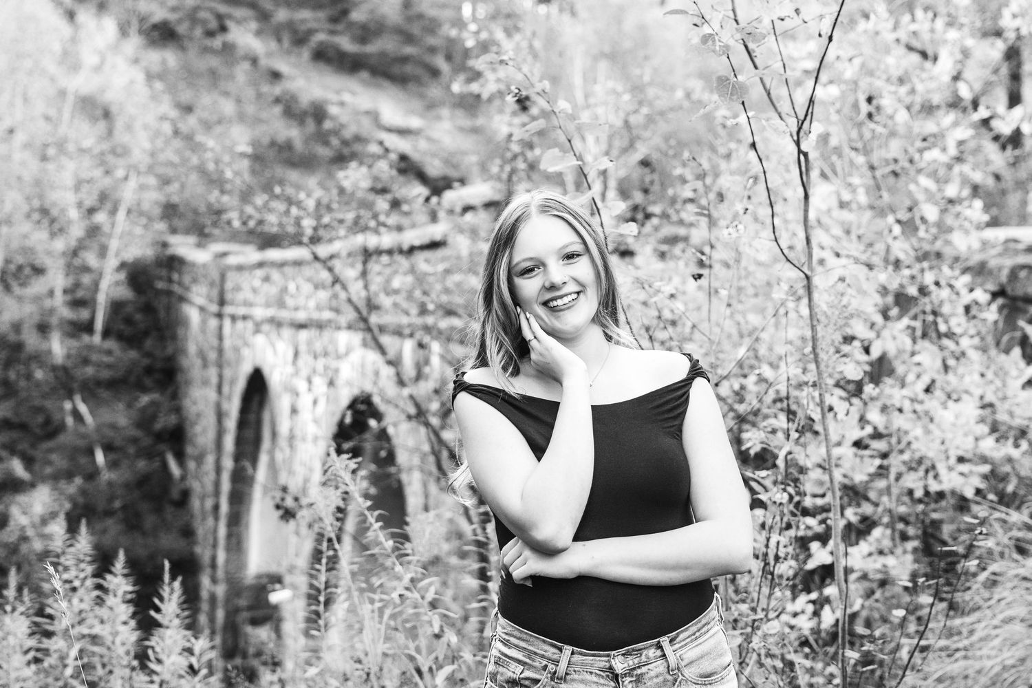 Black and white outdoor portrait session in a natural wooded setting with soft lighting and foliage.