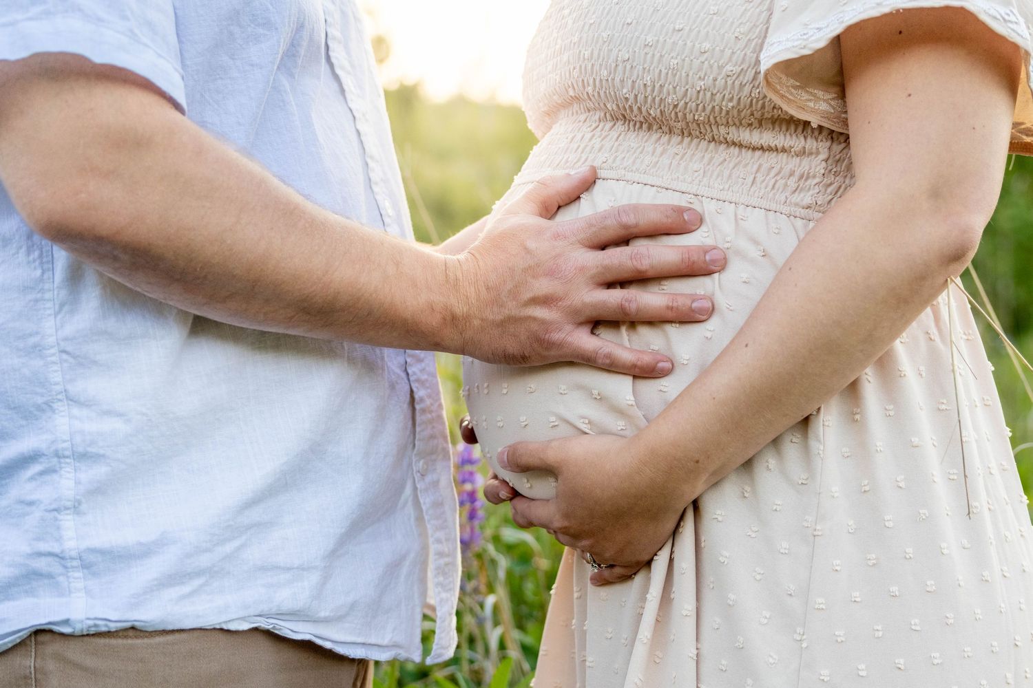 A couple shares a tender moment holding hands in a natural outdoor setting against soft blurred foliage.