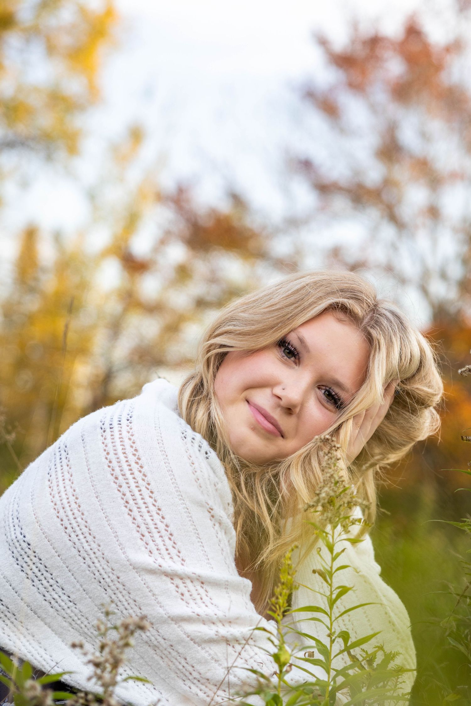 Portrait in white knit sweater outdoors with autumn foliage creating a soft bokeh background in warm colors.