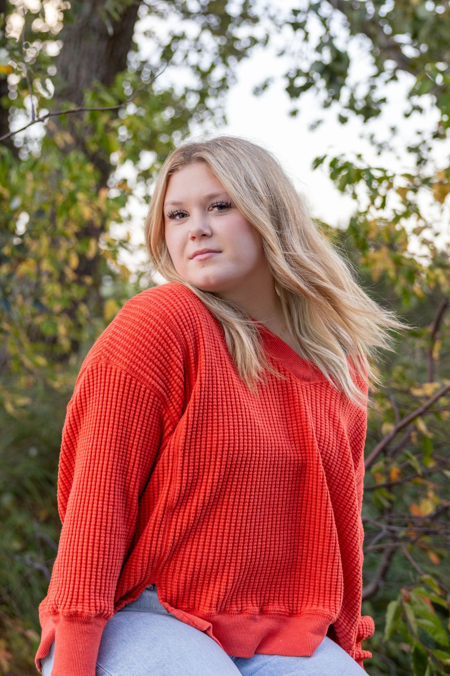 Person in bright red knit sweater poses outdoors against autumn foliage background.