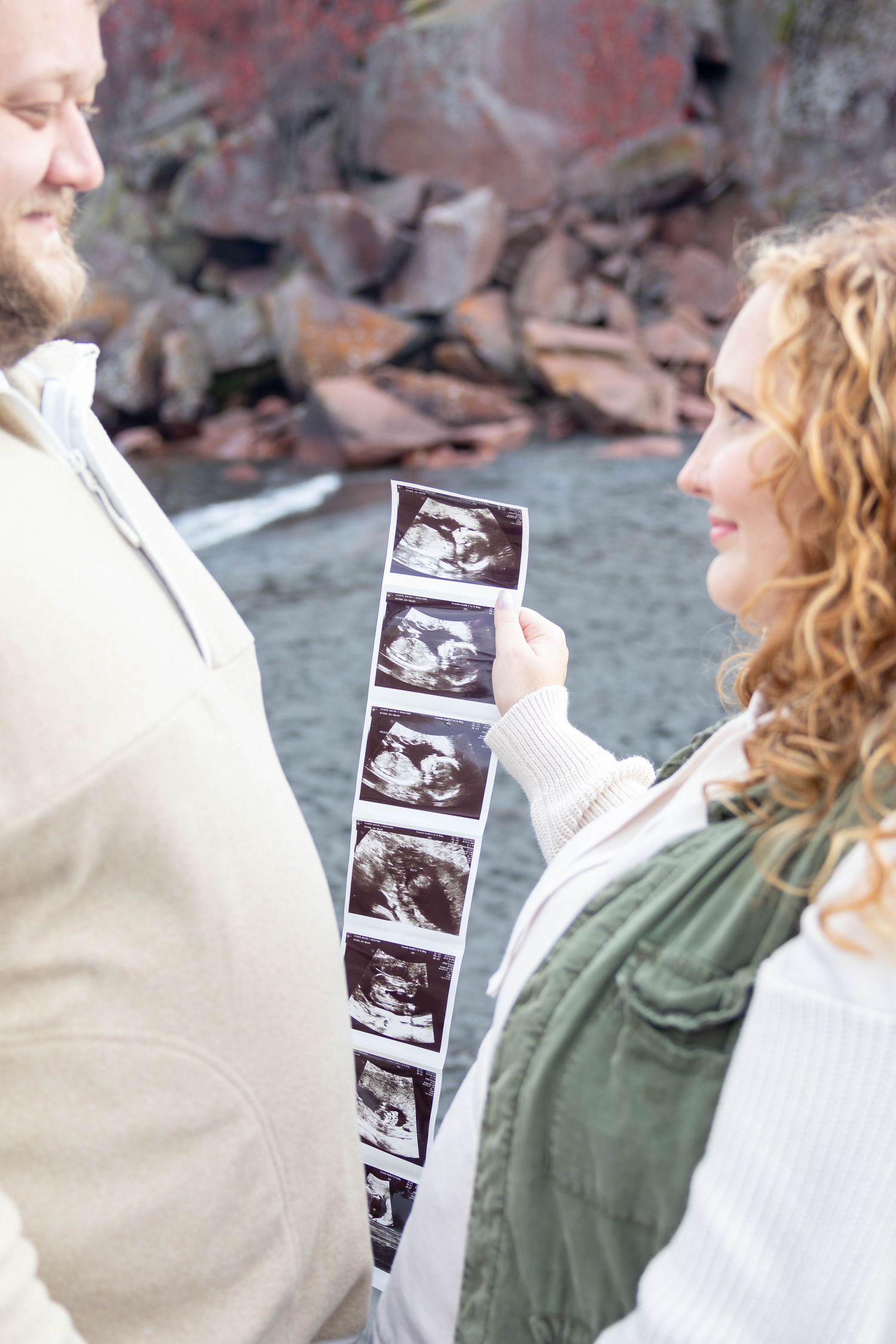 A couple examines ultrasound images together against a rocky coastal backdrop.