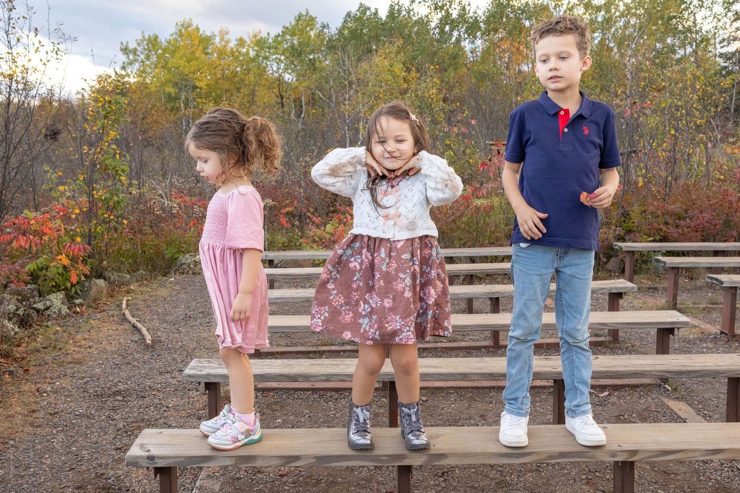 A sequence of people sitting on wooden bleachers in an autumn outdoor setting with fall foliage in the background.