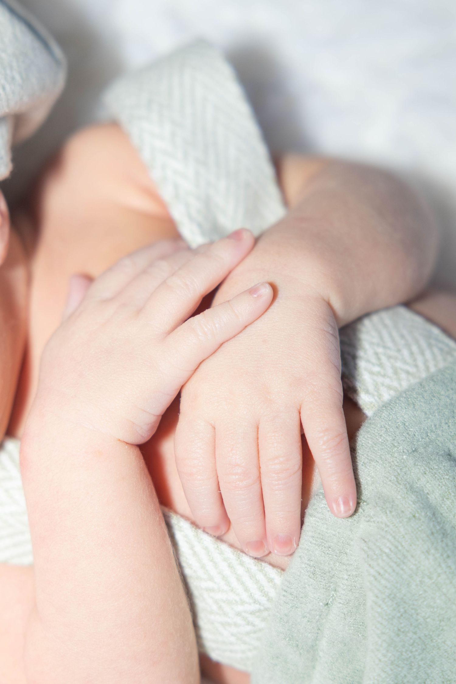 Close-up of tiny baby hand being gently held against white blanket.