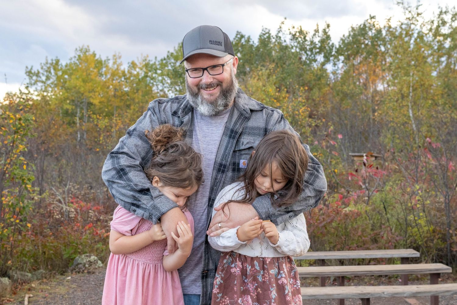 A family shares tender moments together outdoors during autumn with fall foliage in the background.