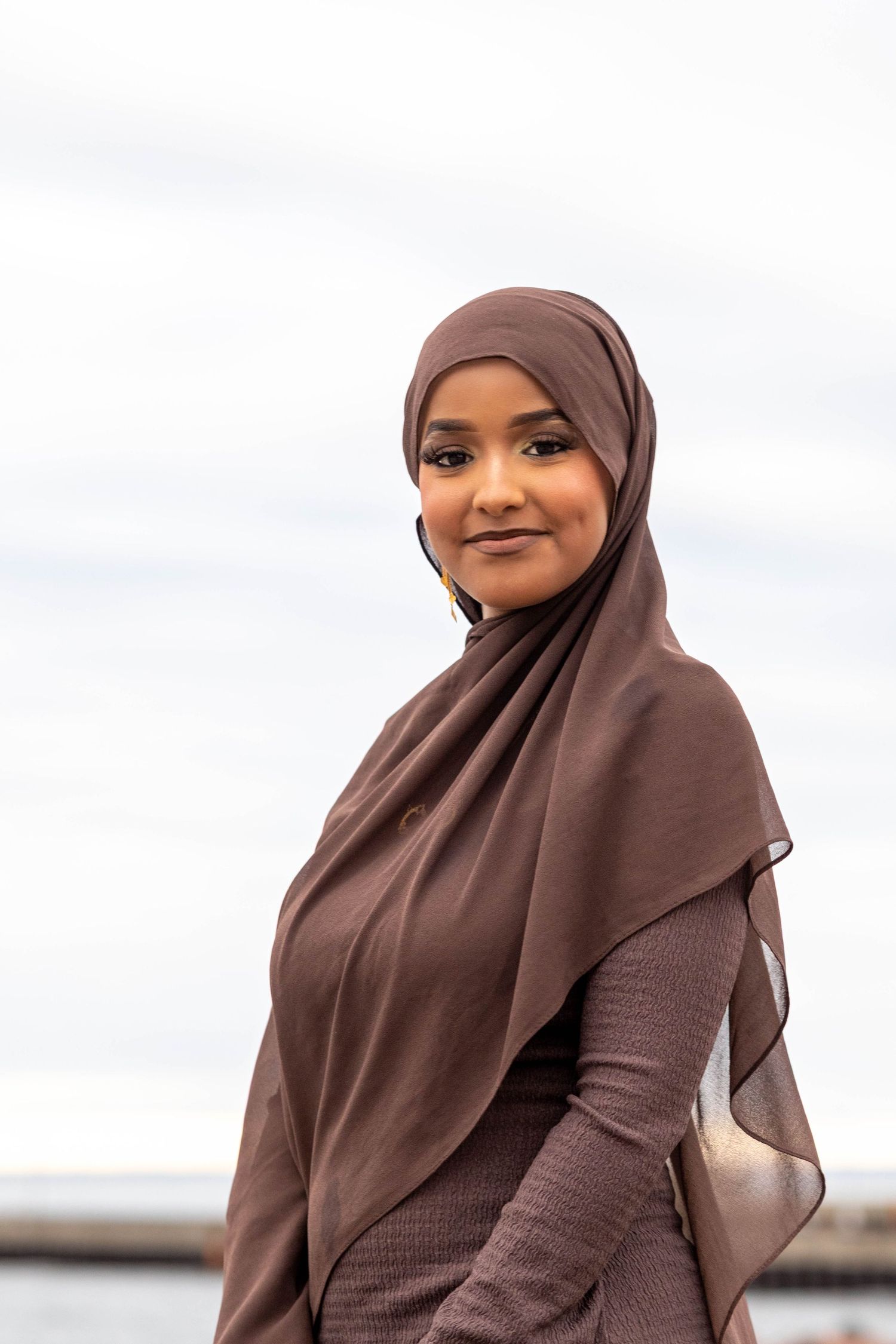 Four portraits of a person wearing a brown hijab and smiling while posing outdoors.