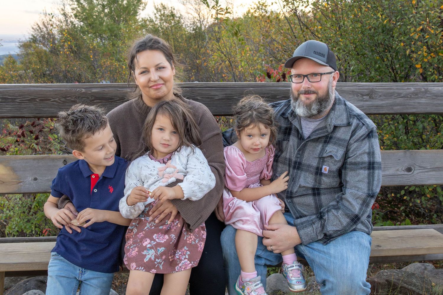 A family sits together on a wooden bench during a fall day in a park setting.