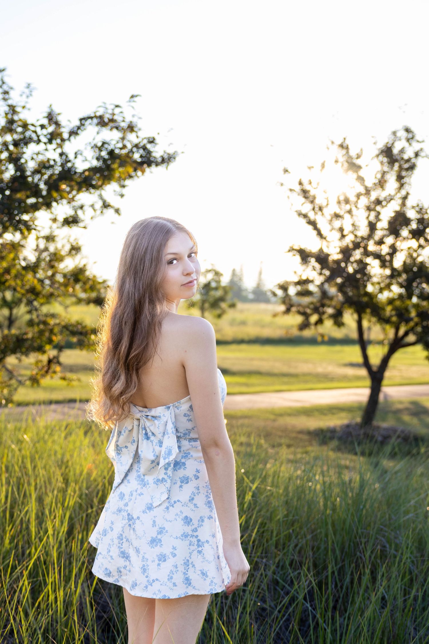 Portrait session in a meadow at sunset featuring woman in blue floral summer top.