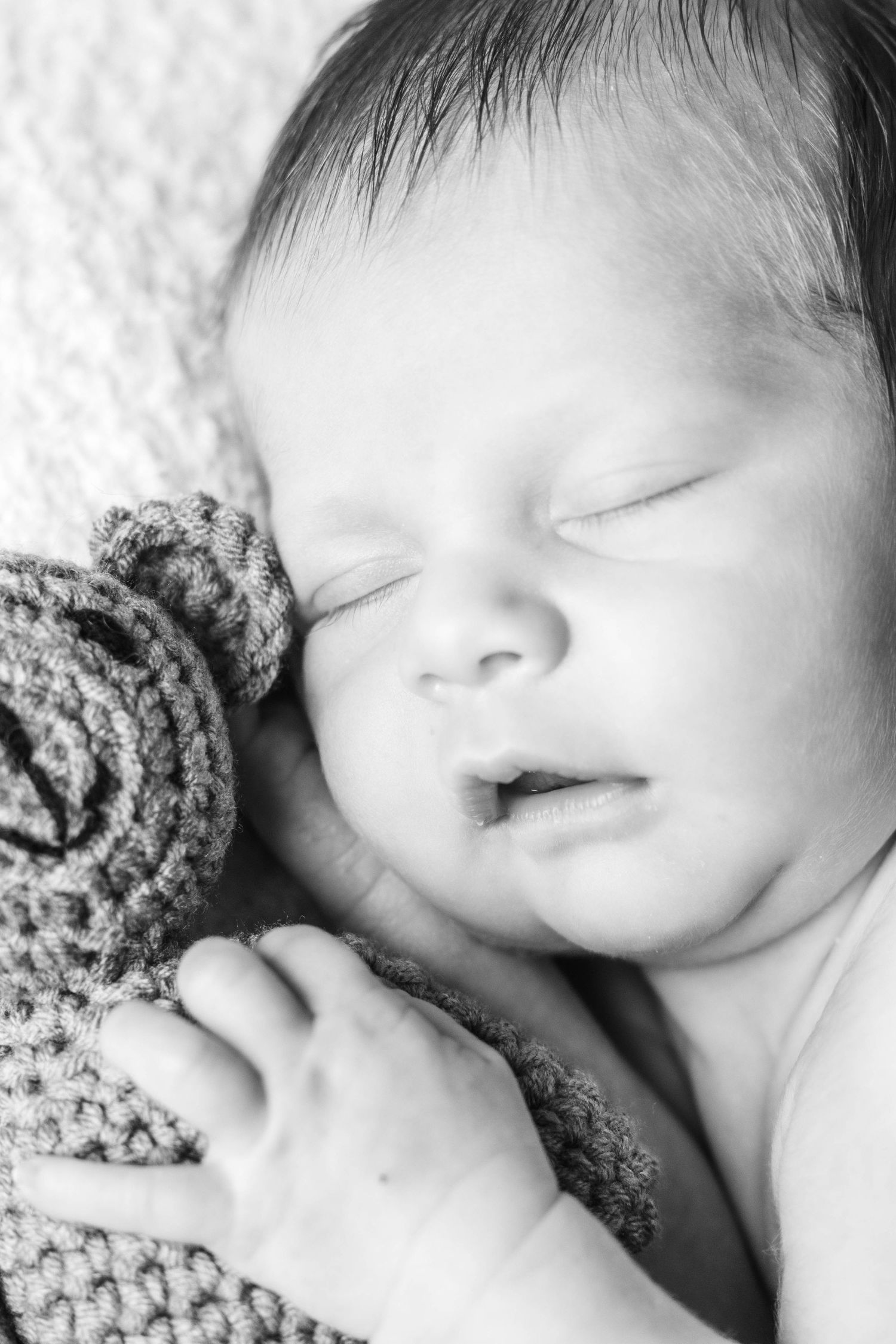Peaceful sleeping newborn wrapped in knitted blanket in black and white portrait.