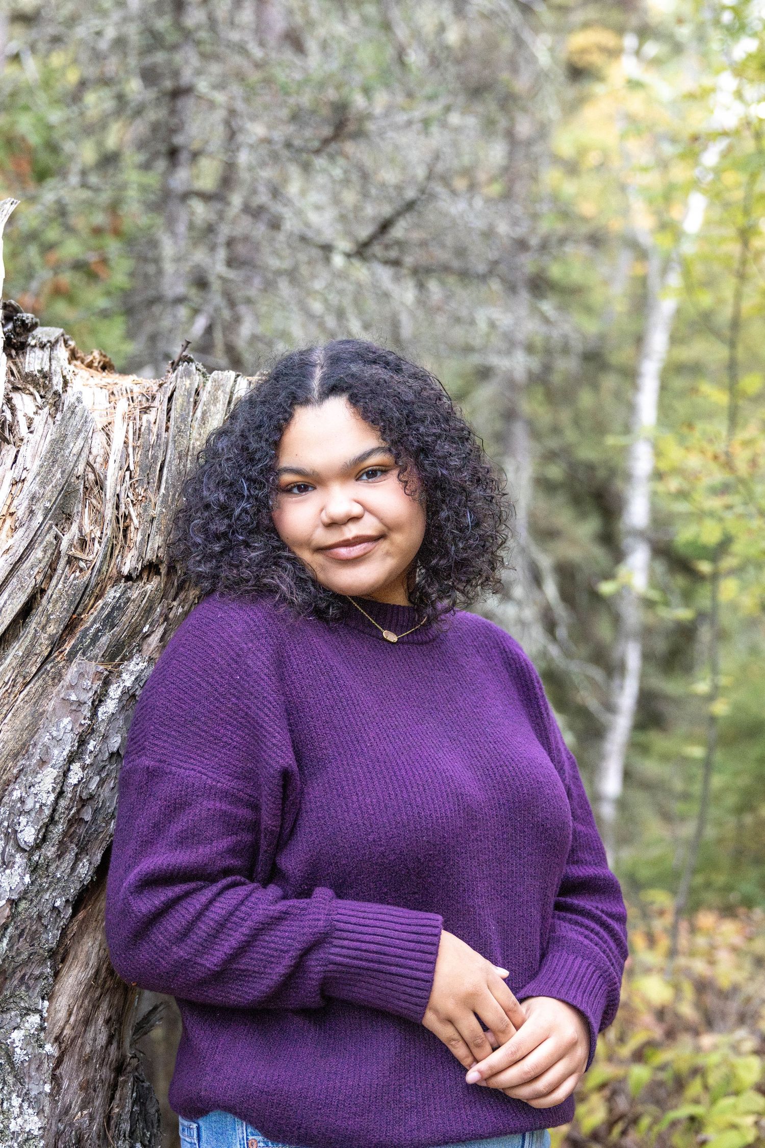 A person in a purple sweater poses against a natural wooded background in a series of outdoor portrait shots.