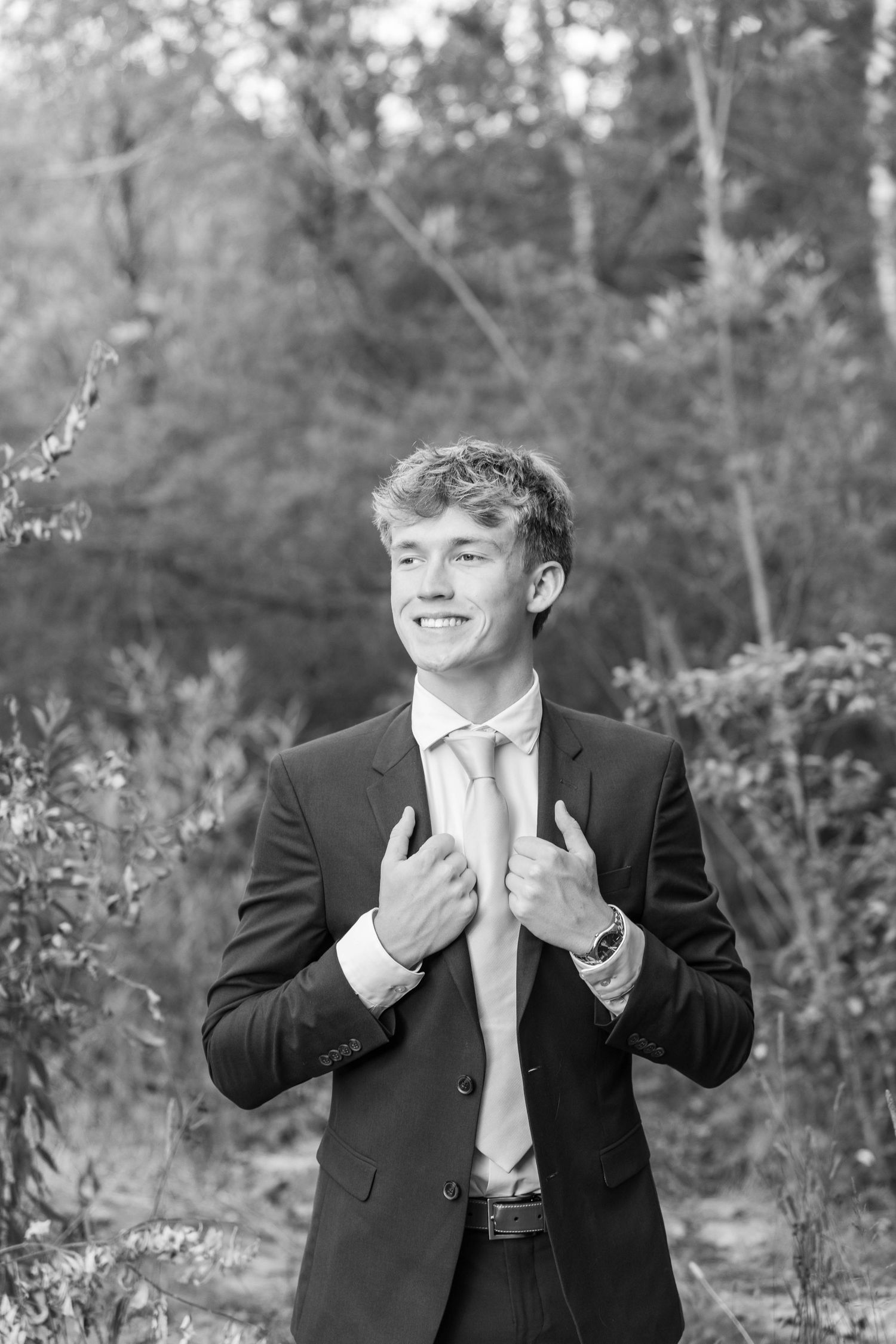 Young man in suit and tie smiling outdoors in black and white portrait photo.