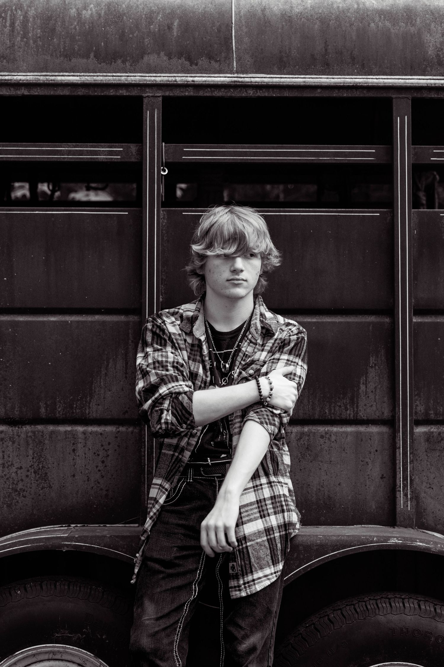 A black and white photo series showing someone in a plaid shirt leaning against a vintage car in different poses.