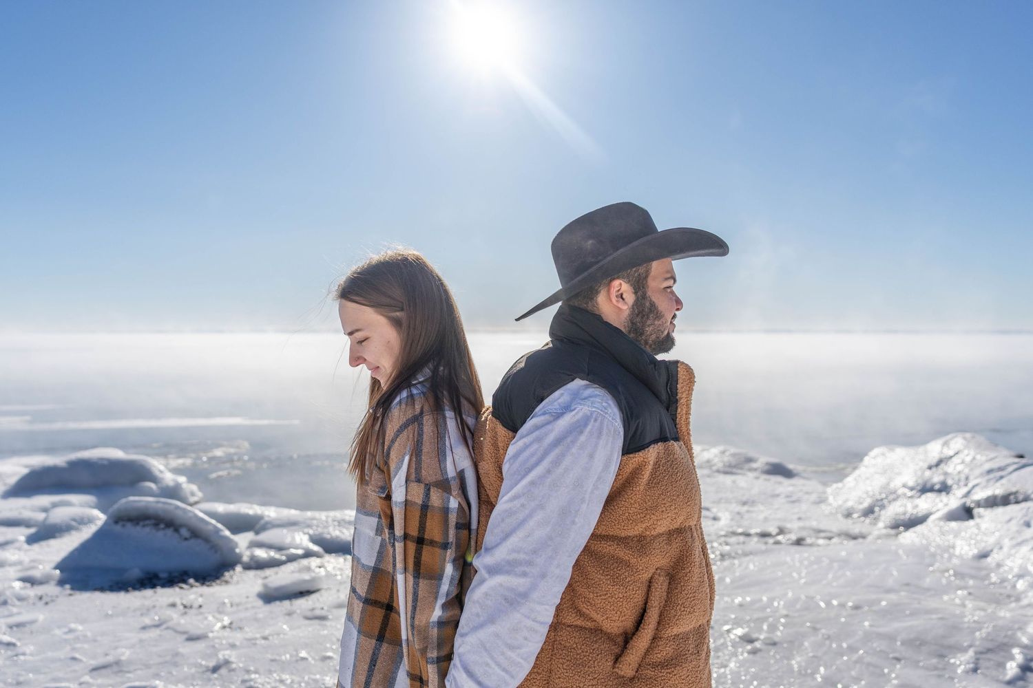 A group stands atop a snowy mountain peak overlooking a vast winter landscape on a bright sunny day.