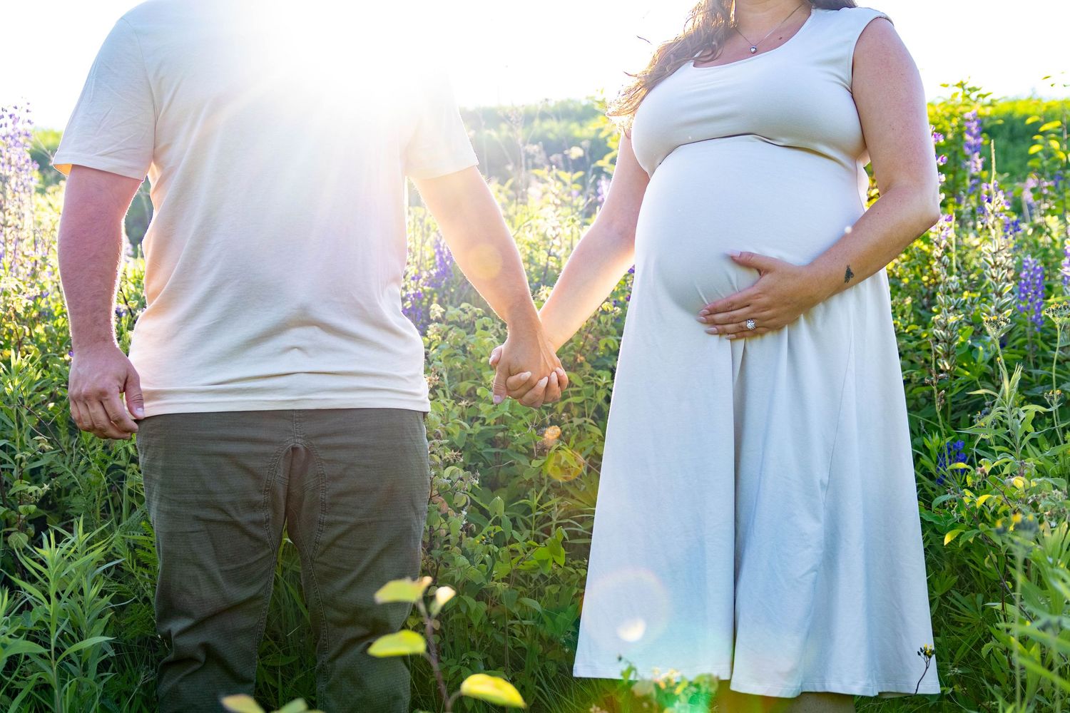 A glowing golden sunlight illuminates several pregnant women in white dresses standing in a garden setting at sunset.