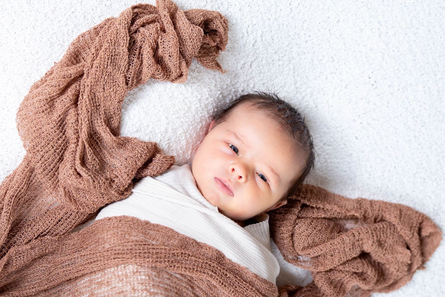A person in a cozy brown sweater lying on a white surface while gazing upward with a contemplative expression.