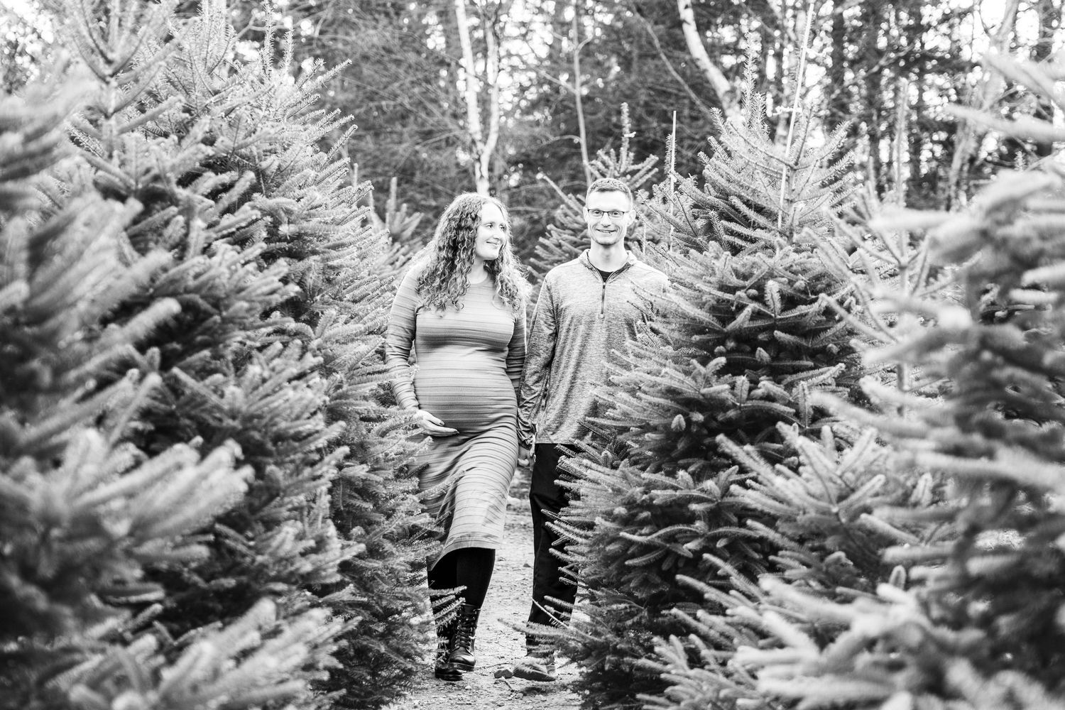 Black and white photograph showing a person selecting a Christmas tree at a snowy tree farm in winter.