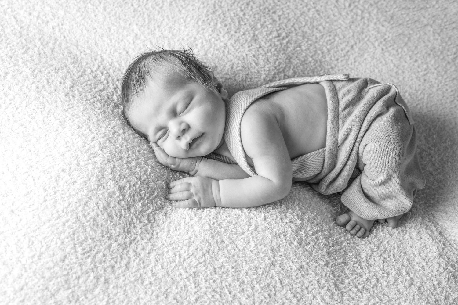 Peaceful sleeping baby in grey outfit on white carpet, black and white photo.