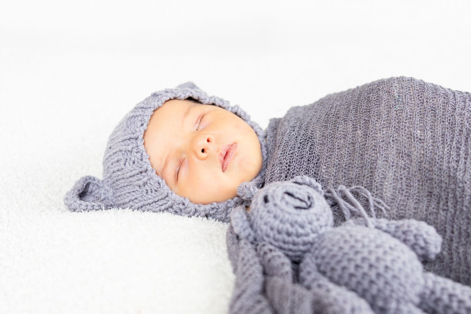 A baby sleeping peacefully while wearing a cozy gray knitted outfit with bunny ears.