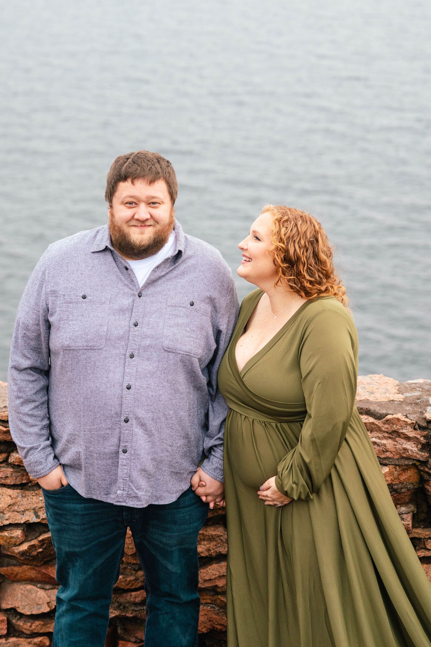 Happy couple sharing intimate moment during coastal maternity photoshoot.