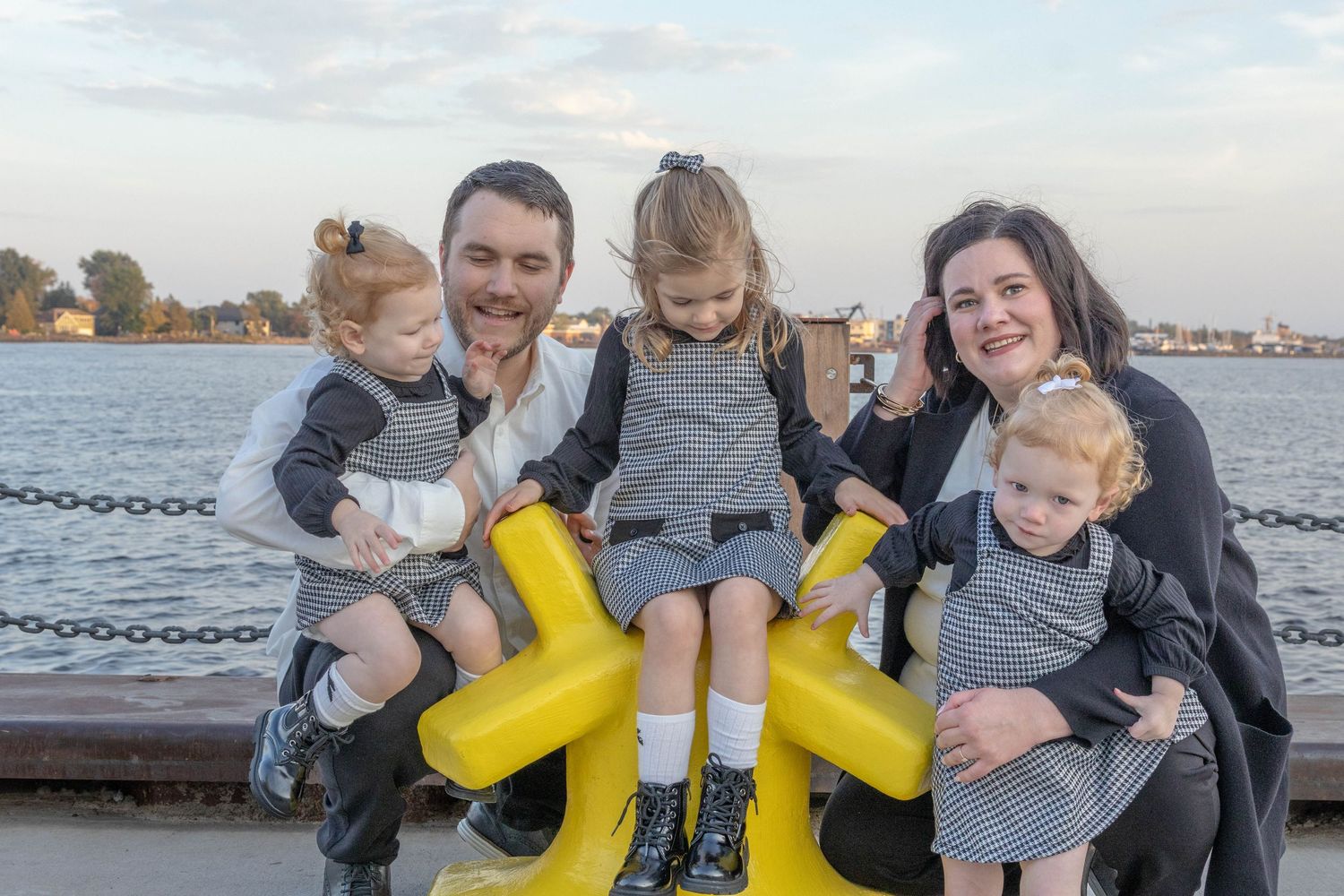 A family wearing yellow rubber boots poses together on a wooden dock by the water on a cloudy day.
