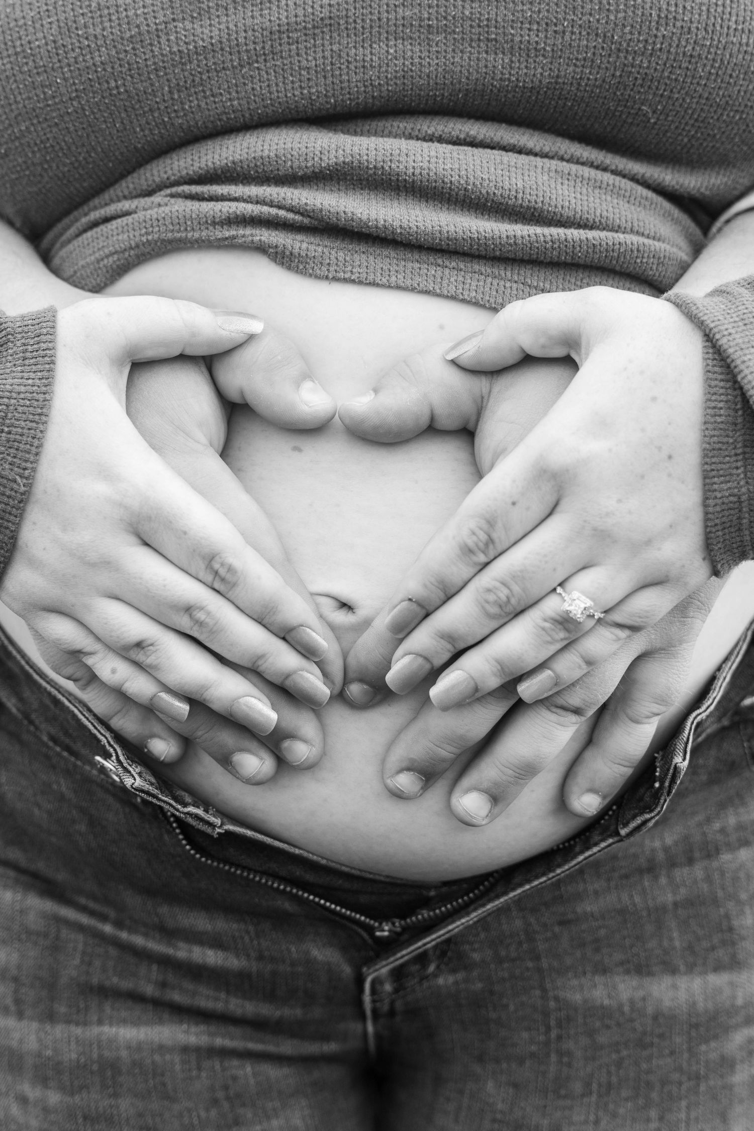 Hands form a heart shape over a pregnant belly in black and white.