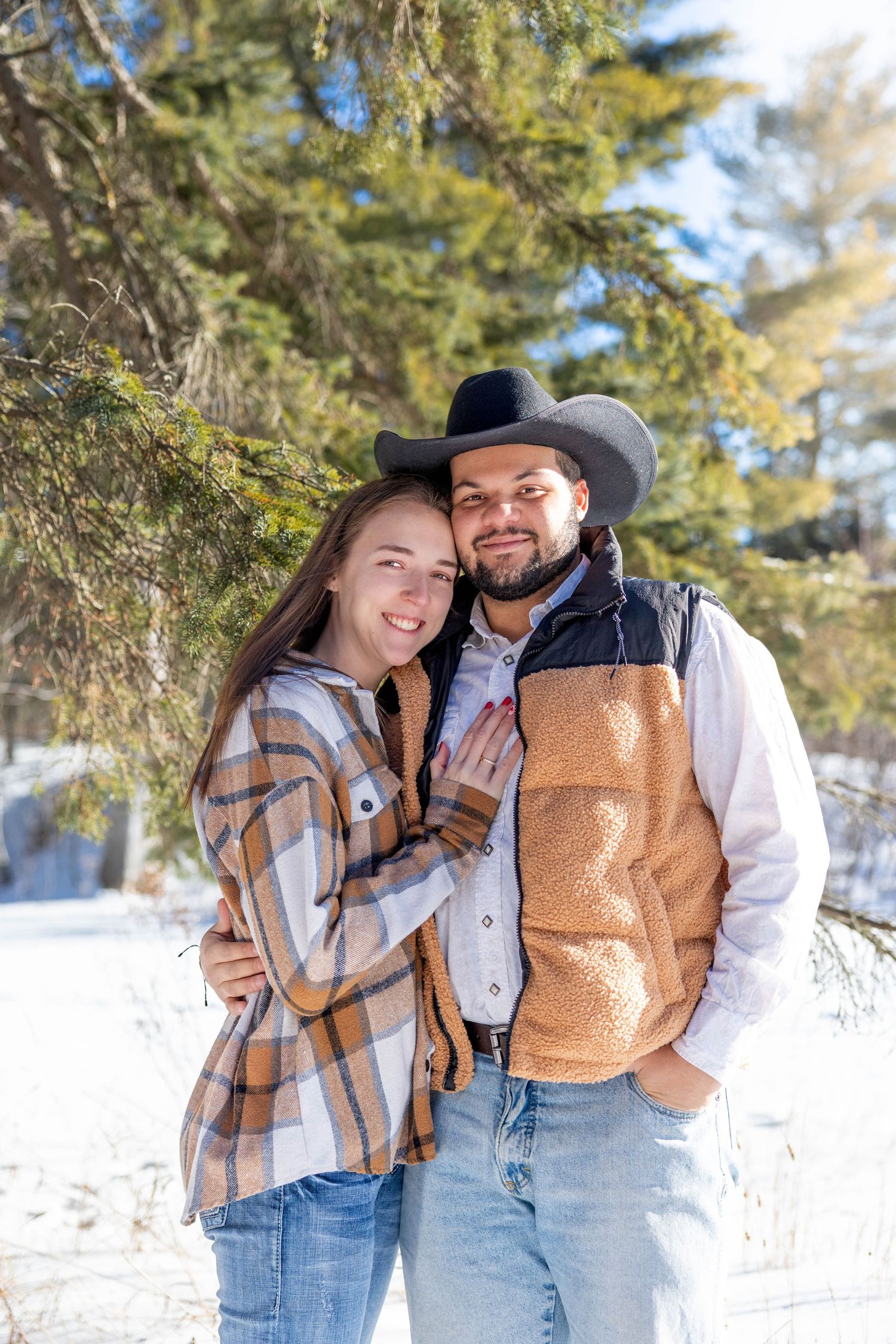 Couple in matching plaid and denim outfits pose together in snowy winter forest setting.