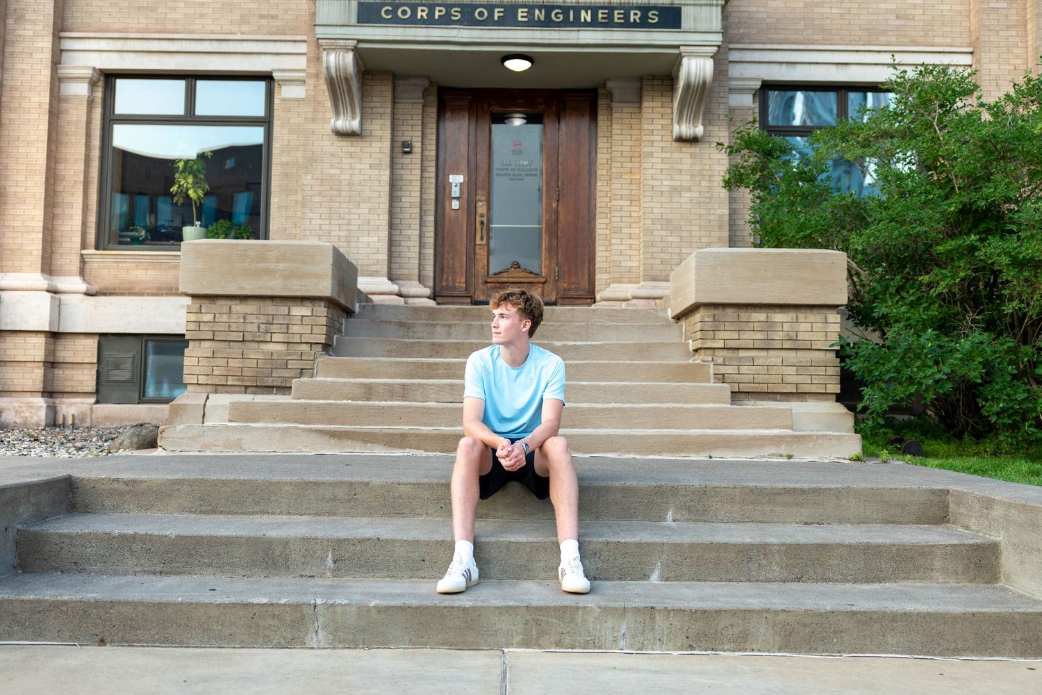 Teen boy in blue shirt sits on steps of Corps of Engineers building for a portrait photo.