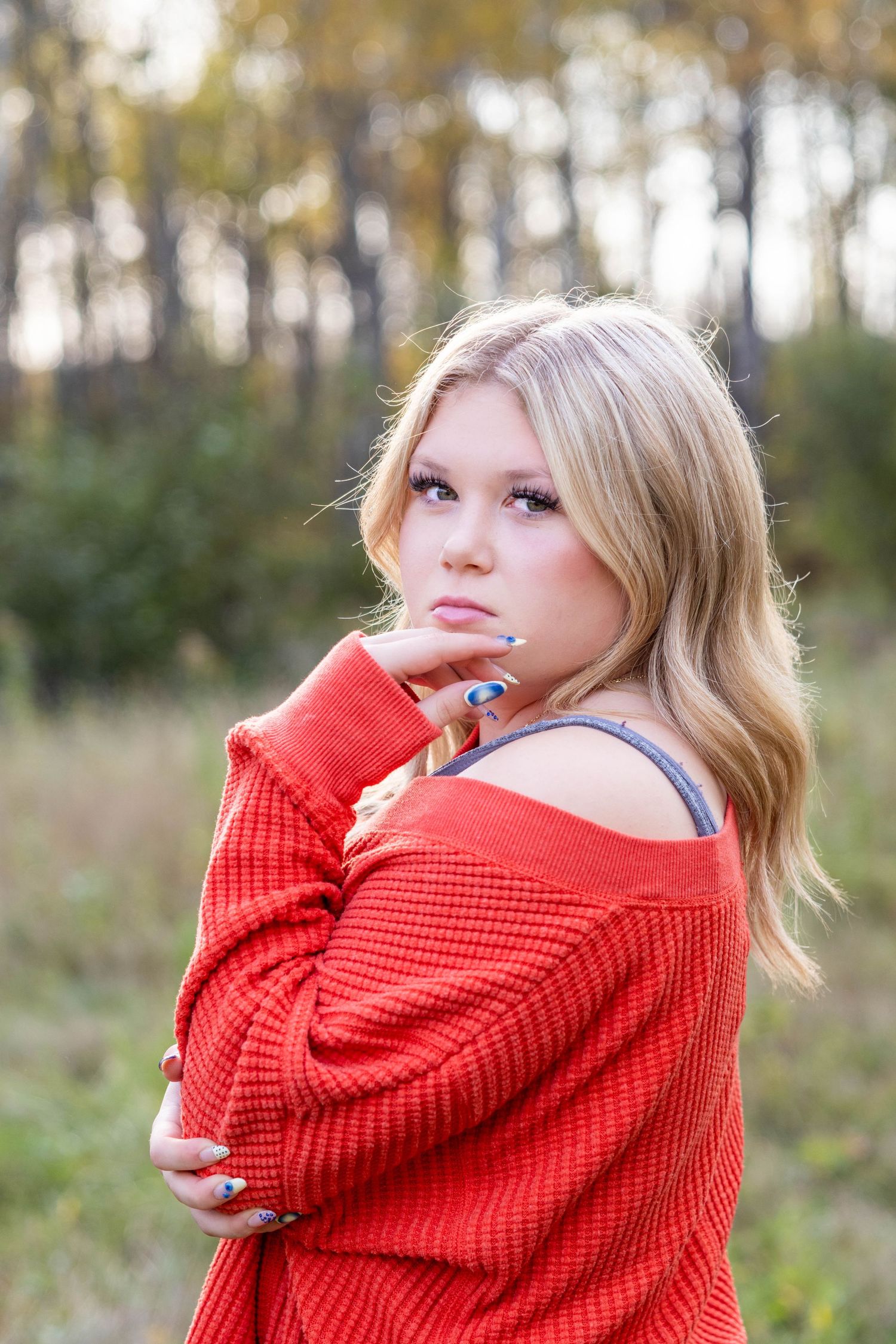 A person in a cozy red knit sweater poses outdoors in an autumn setting with trees and natural light.