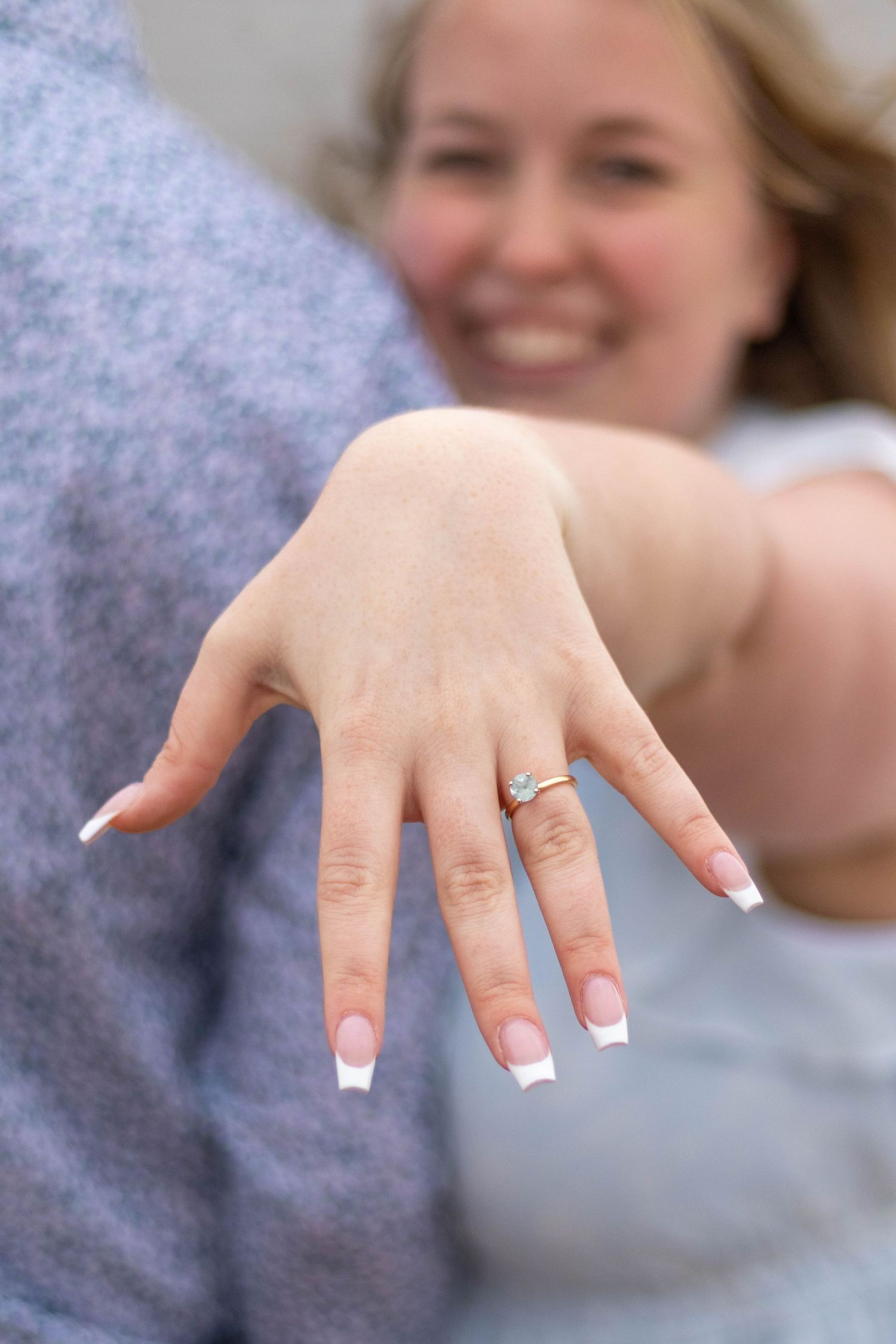 Close up of a hand showing off a diamond engagement ring with French tip manicured nails.