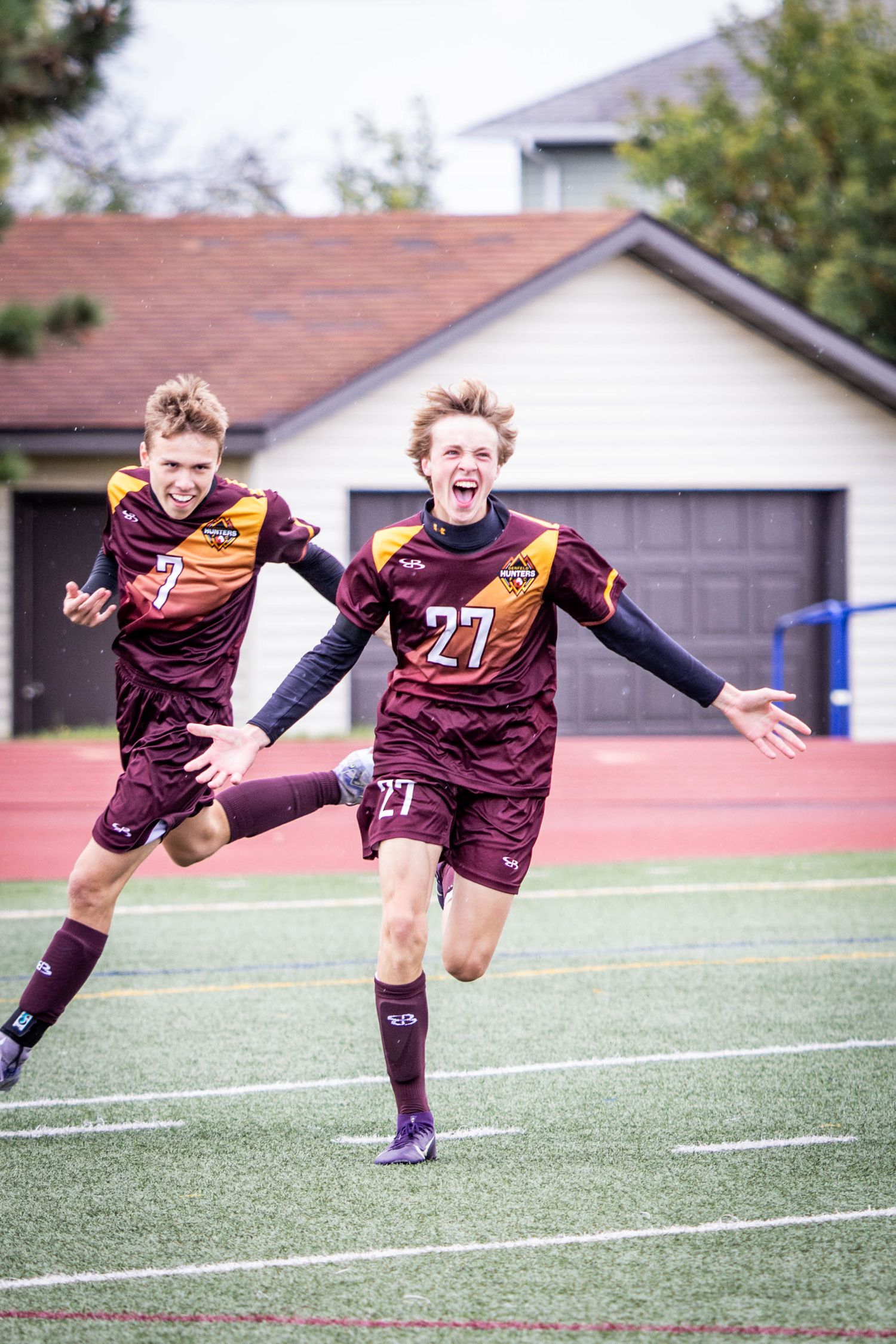 Young soccer players in maroon and purple uniforms leap and jump in celebration on a turf field.