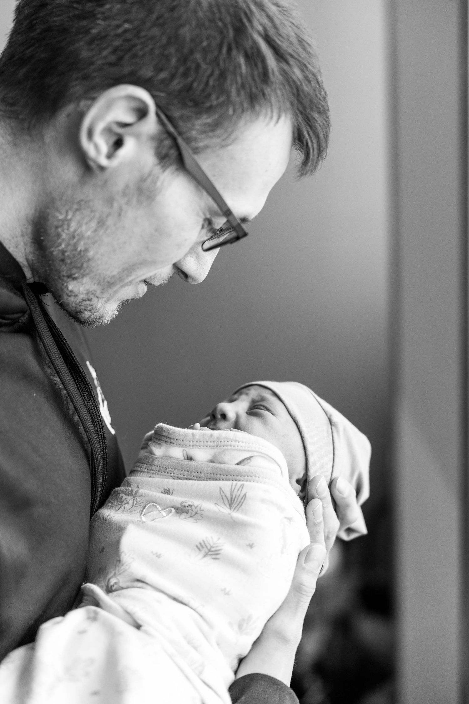 A tender black and white photo series showing a parent holding and bonding with a newborn baby in white clothing.