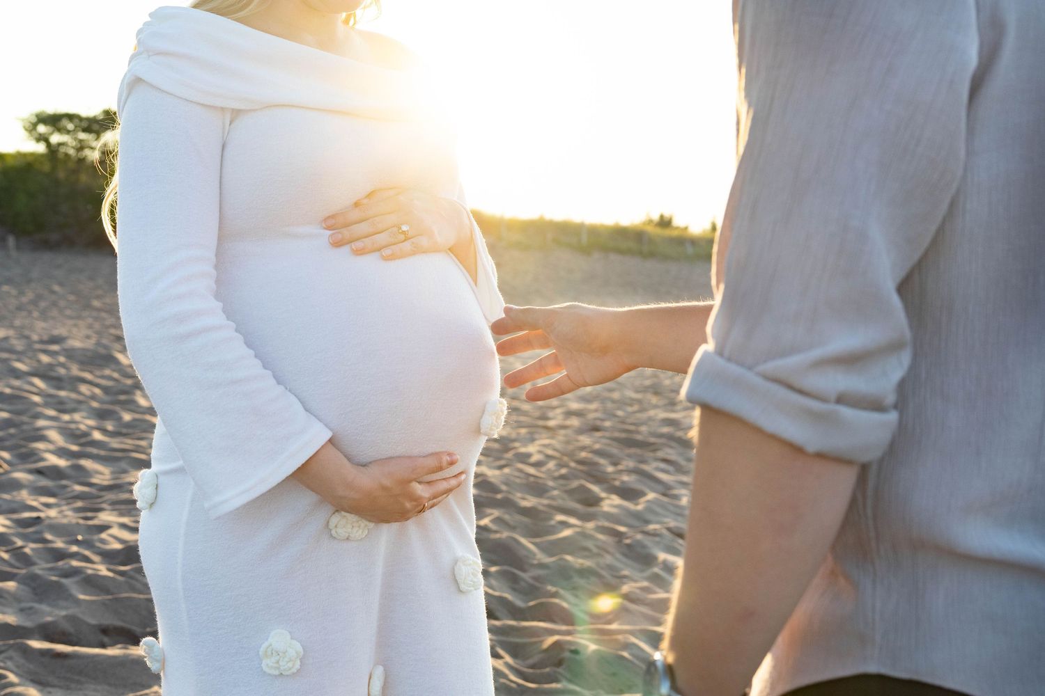 Intimate maternity photo shoot with couple embracing on sunny beach at golden hour.