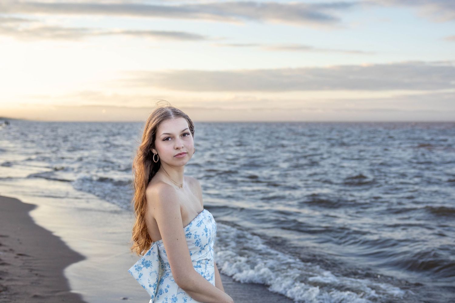 Woman in floral dress poses along scenic ocean coastline at sunset creating dreamy beach portraits.