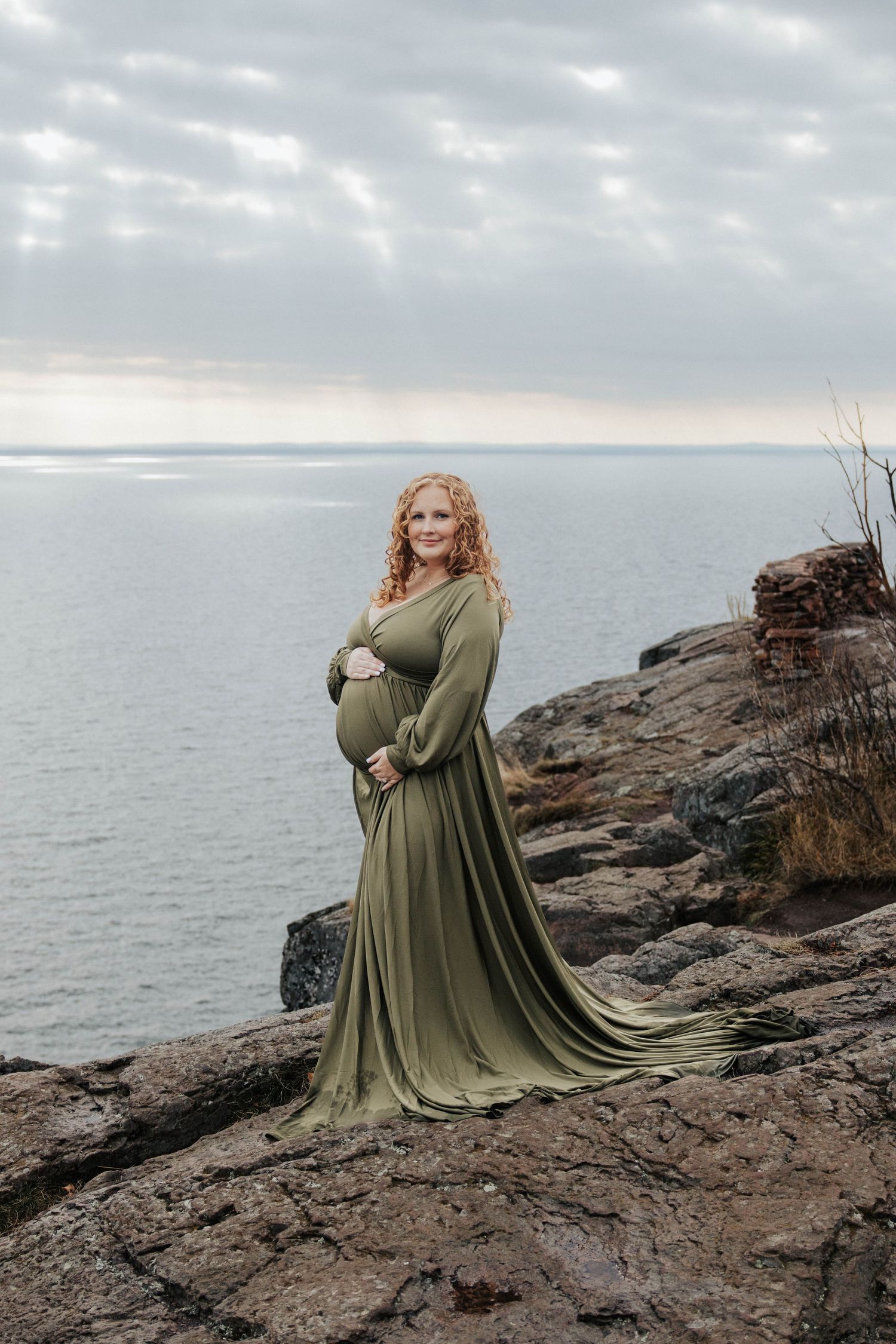 Flowing green dress creates dramatic silhouette in coastal maternity photo.