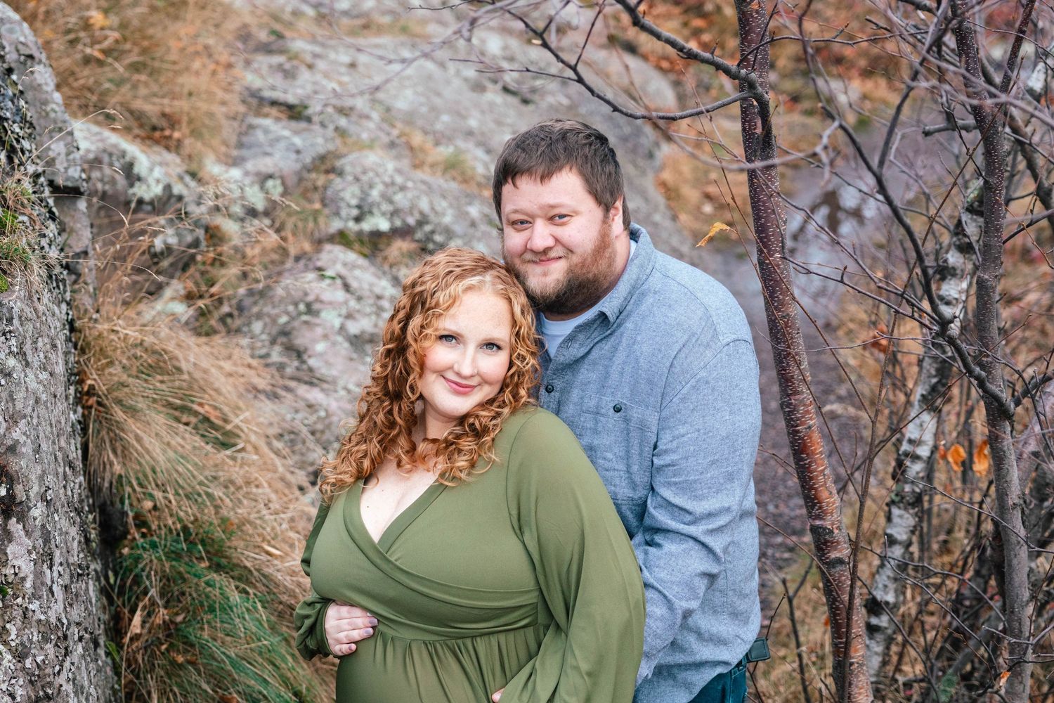 A couple poses together in an outdoor setting with rocky terrain and bare trees in the background.