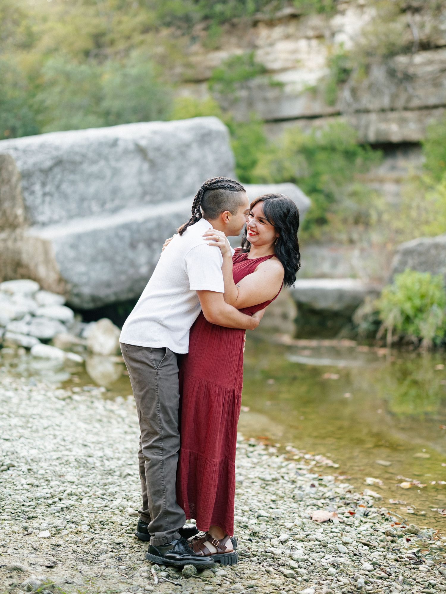 Couple embracing and smiling on a rocky riverbank surrounded by natural stone cliffs.
