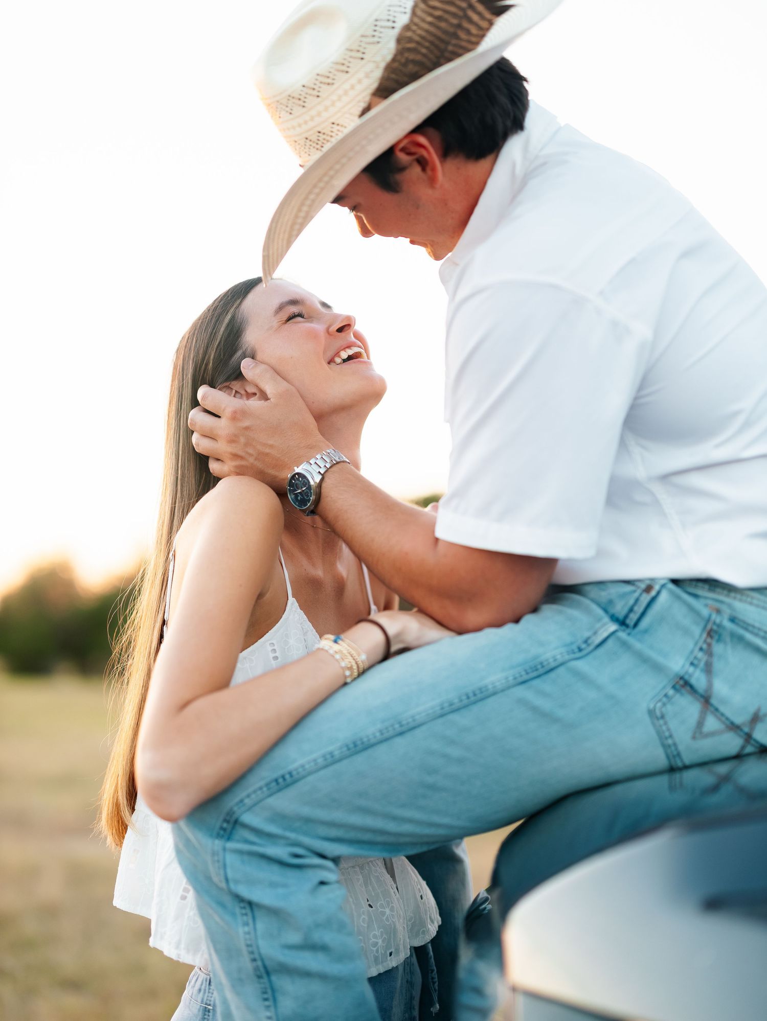 A couple shares a romantic moment at golden hour, man in cowboy hat gently holding womans face.