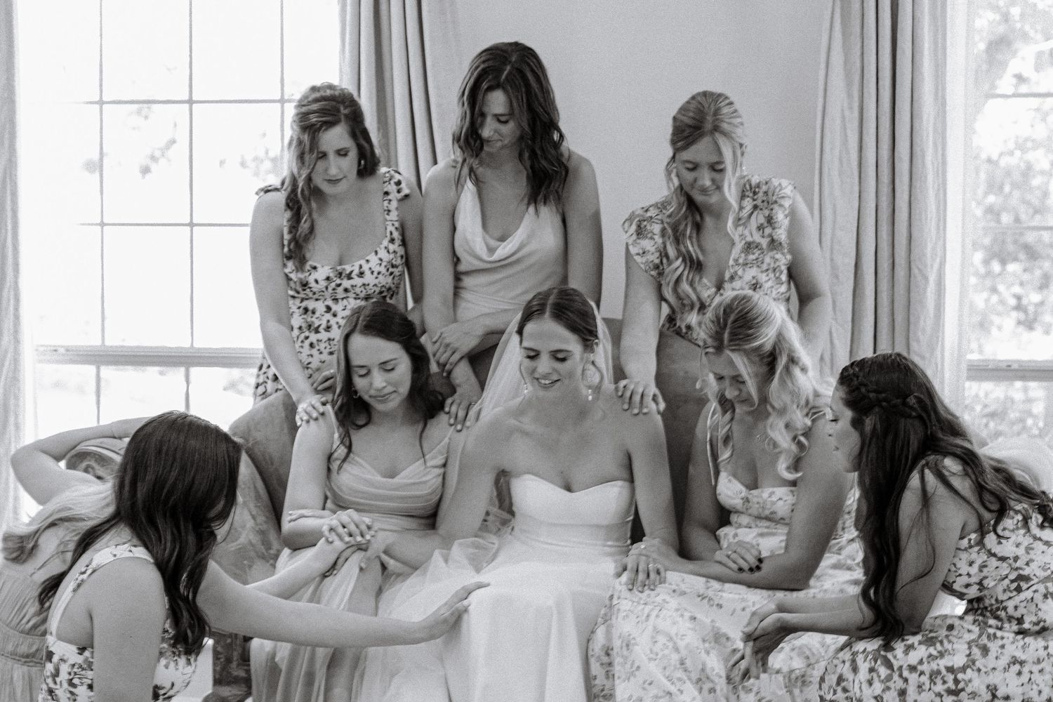 Black and white image of wedding party praying together around the bride.